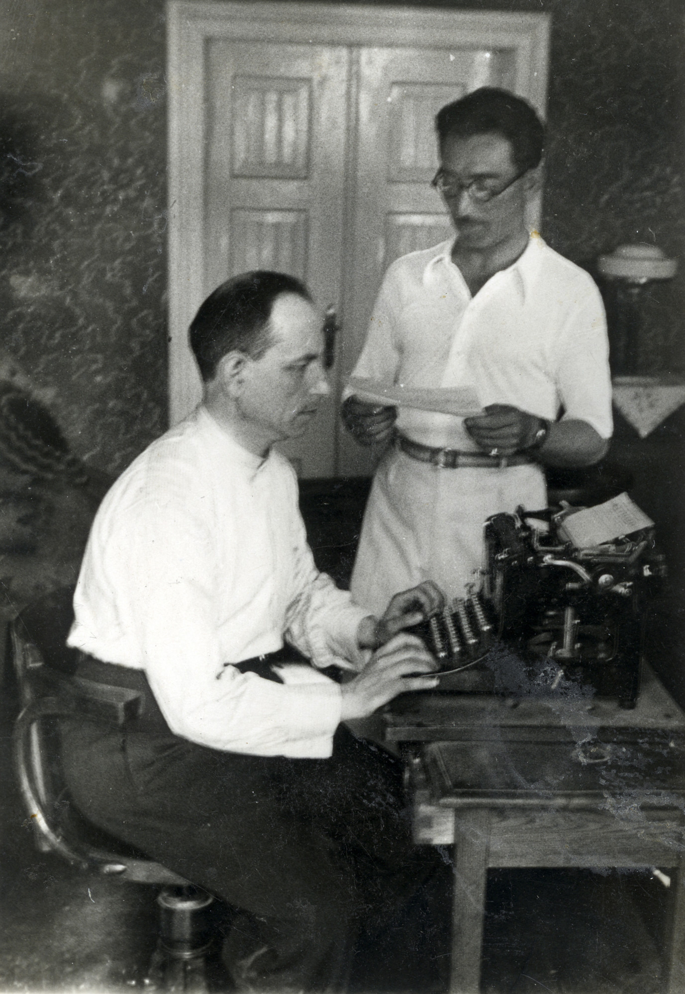 Moshe Alterman works in the office of his furniture factory, standing next to  his accountant seated at the typewriter.