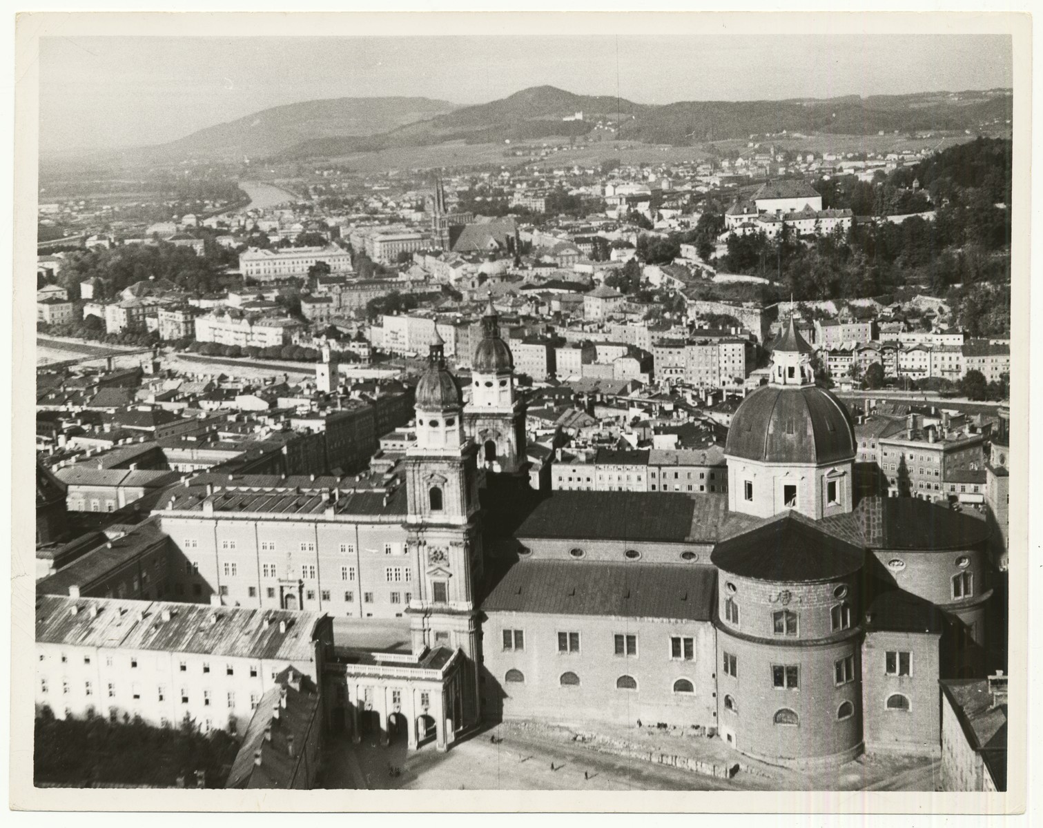 A view from Hohensalzburg Fortress in Salzburg, Austria.  In the foreground is the Salzburg Cathedral.

The handwritten caption on the back of the photograph reads: "Salzburg, Austria, view from Fortress Hohensalzburg.  In foreground the Dom (Cathedral), in front of which the "Everyman" (Jedermann) performances during the Salzburg festival take place."