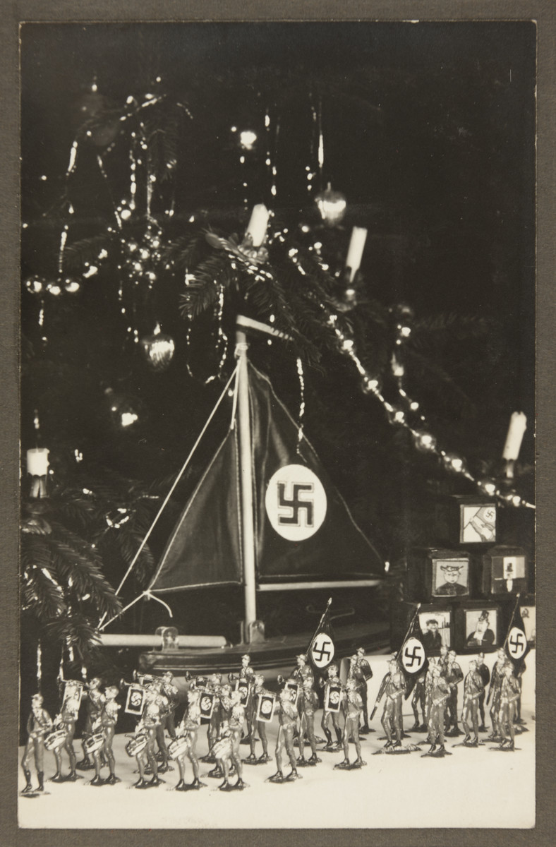 Children's toys, including tin Nazi stormtroopers and a toy ship with a Nazi flag are displayed before a Christmas tree.