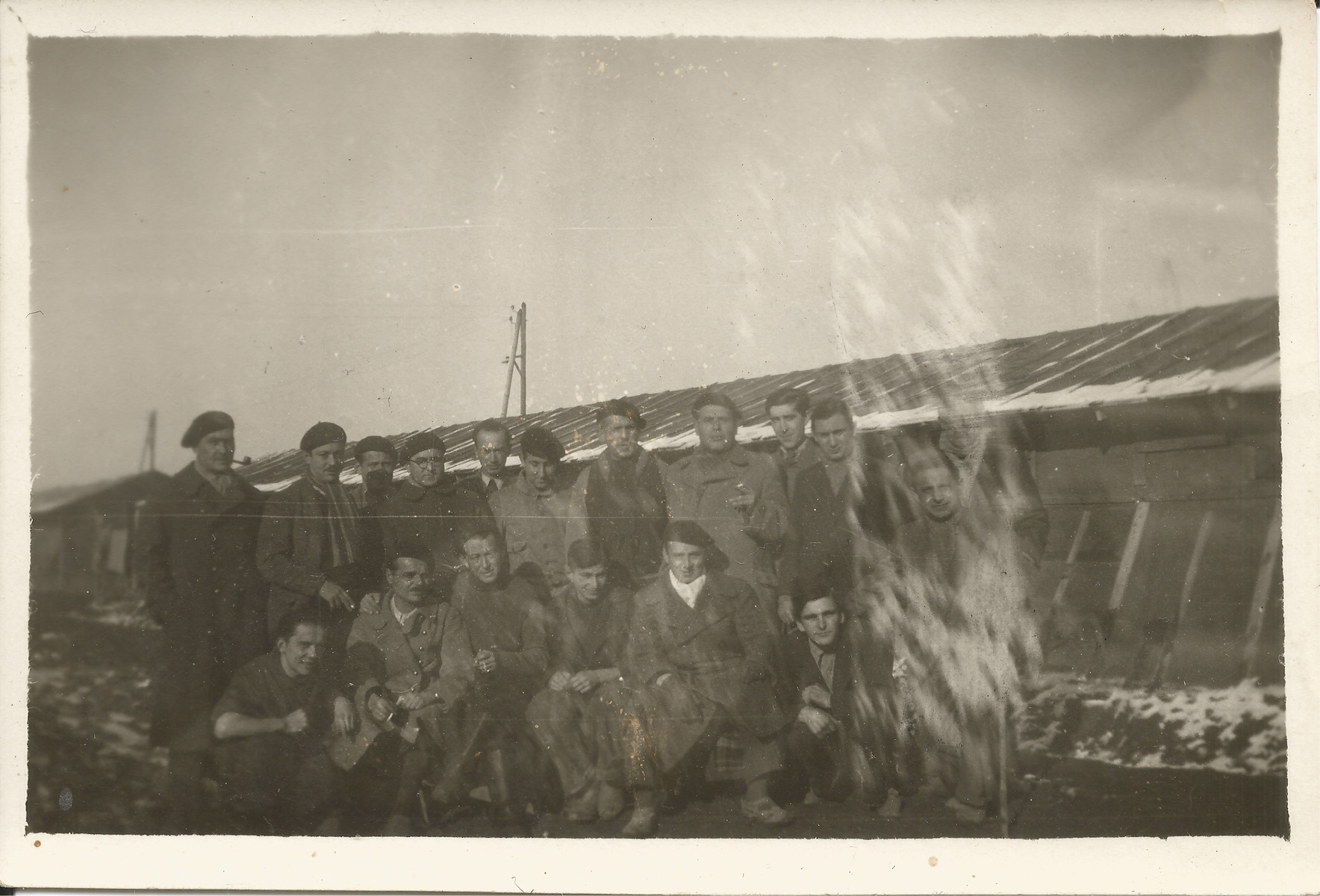 Group portrait of internees in the Gurs camp posing outside their barrack.  

Among those pictured is Siegfried Lindheimer (first row, fifth from the left).