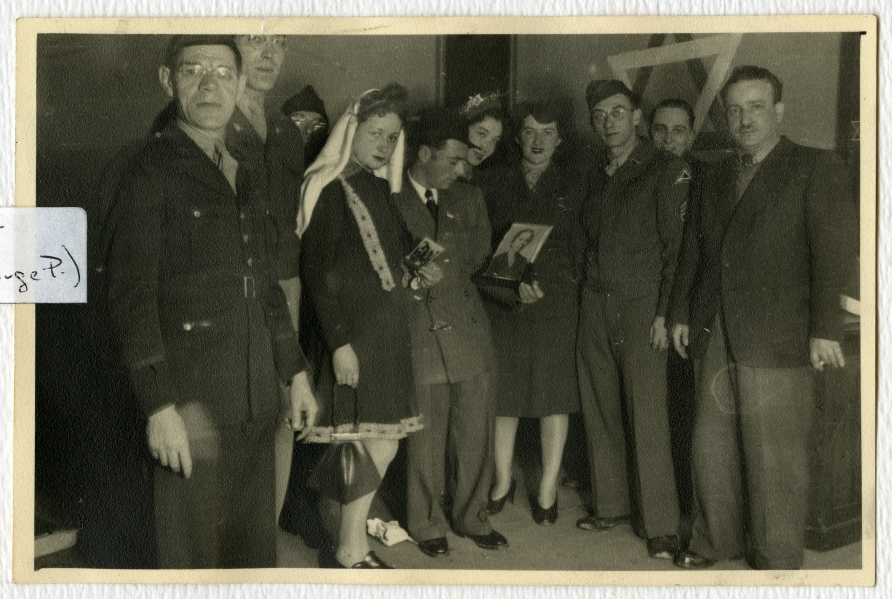 Mr. and Mrs. Pressman hold the photographs of relatives who perished during their wedding in the Stuttgart dsiplaced persons camp.

Cantor Moses Rontal is standing on the far right.