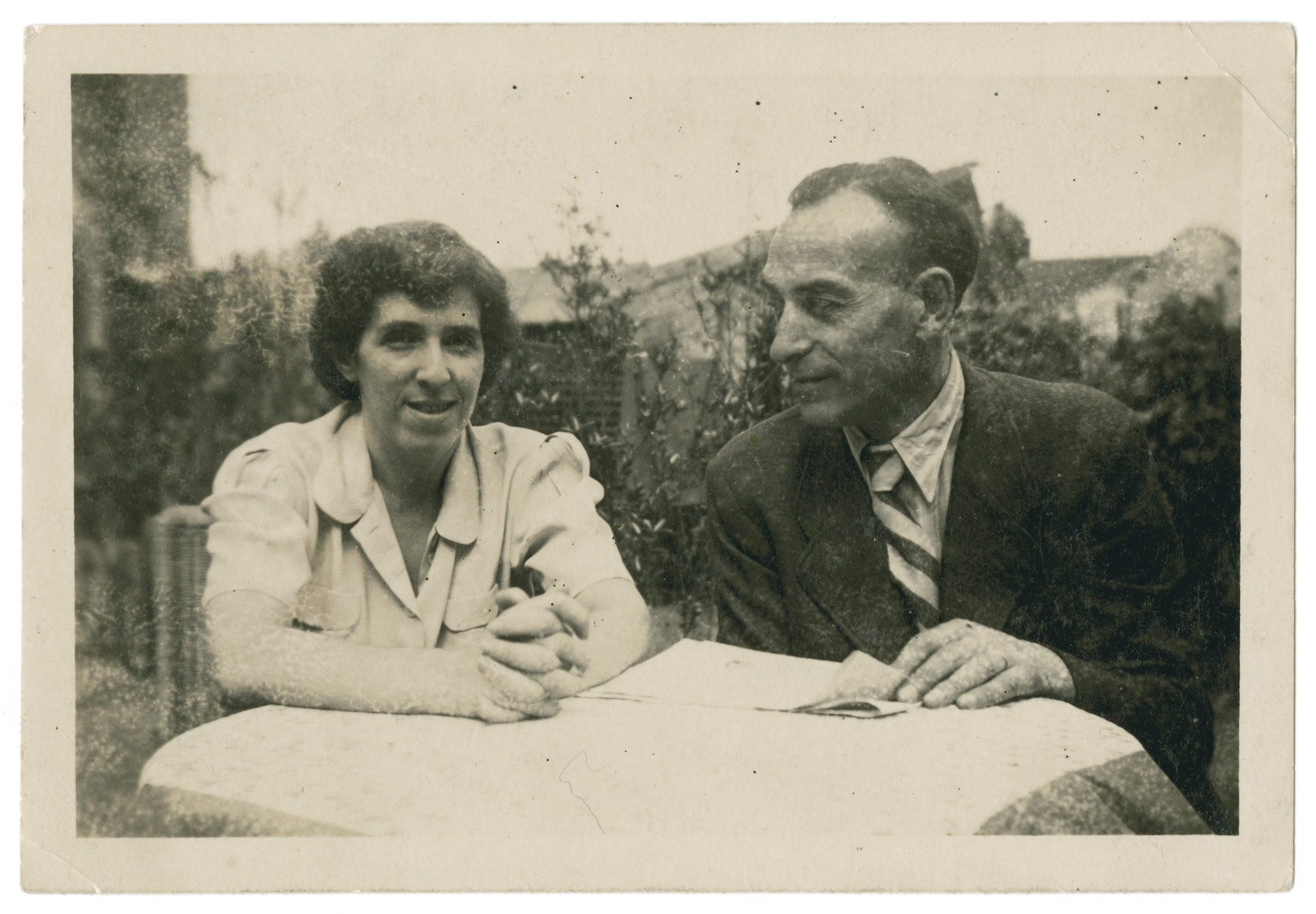 Jewish refugees Max and Erna (nee Weissblum) Pikarski (aunt and uncle of the donor) sit at an outside table in Shanghai.

They formerly lived in Neurode, Schlesien.  After the war both came to Oakland, California with many members of their family who had fled Germany to Shanghai.