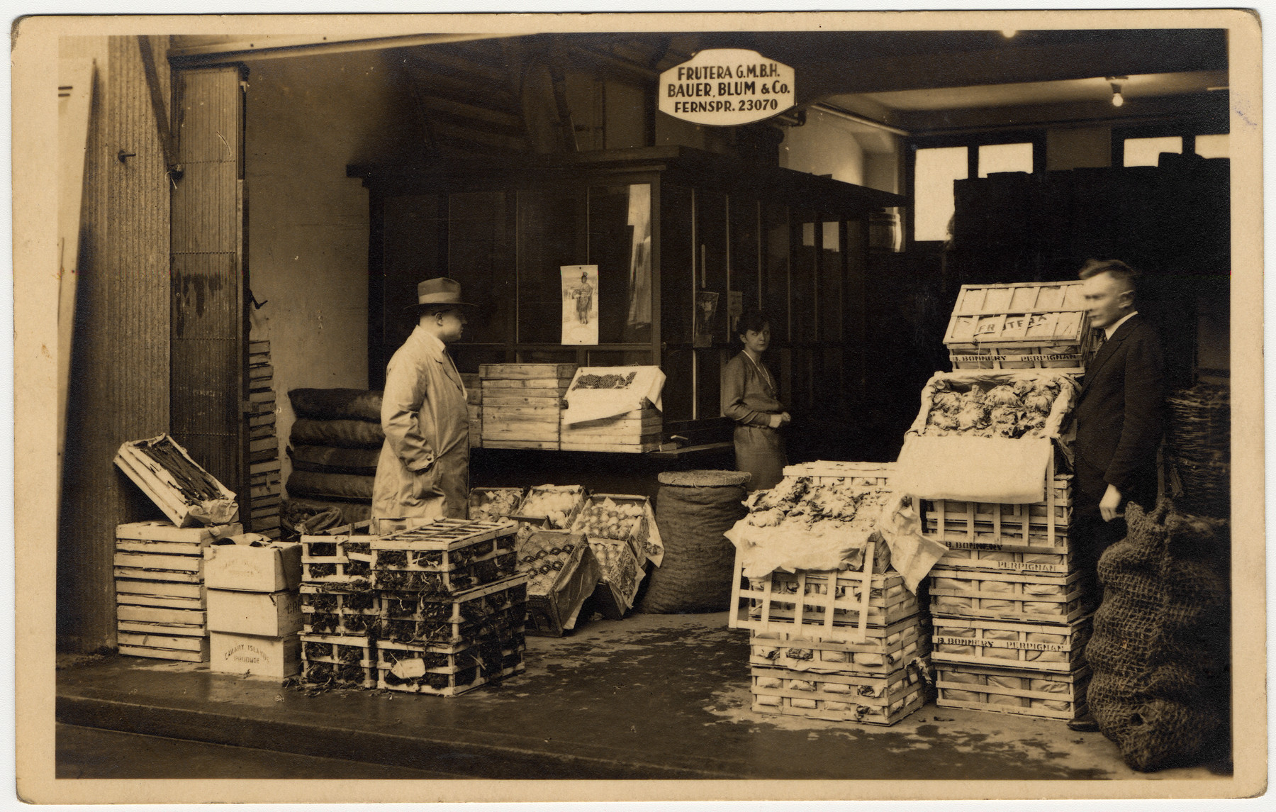 Two men and a woman work instide the Bauer, Blum and Co. Frutera amid crates of fruit and vegetables.