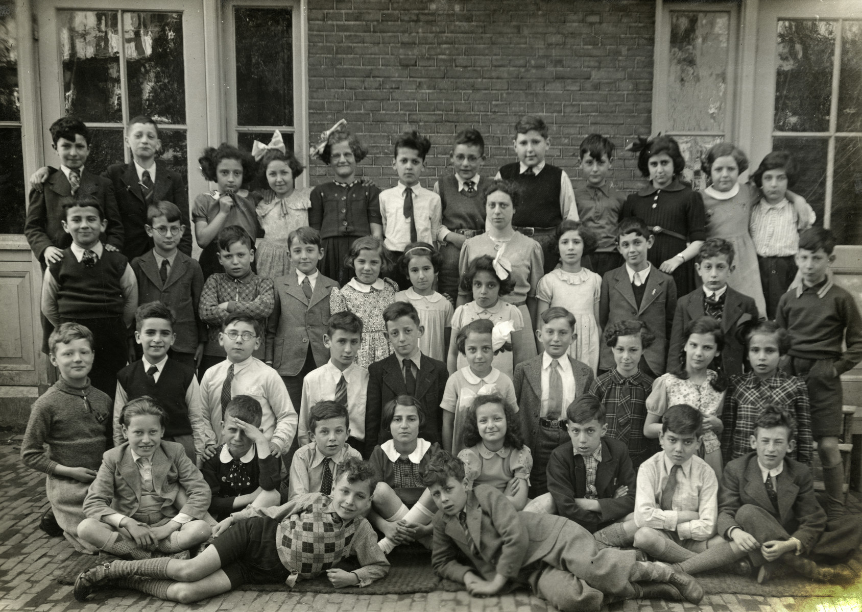Group portrait of children in the 3rd grade of the Jewish elementary class in Amsterdam.

Among those pictured are Elchanan Tal (front row in a while shirt and tie), Hetty d'Ancona deLeeuwe (back row, second from right), and Judith Konijn (back row, far right).