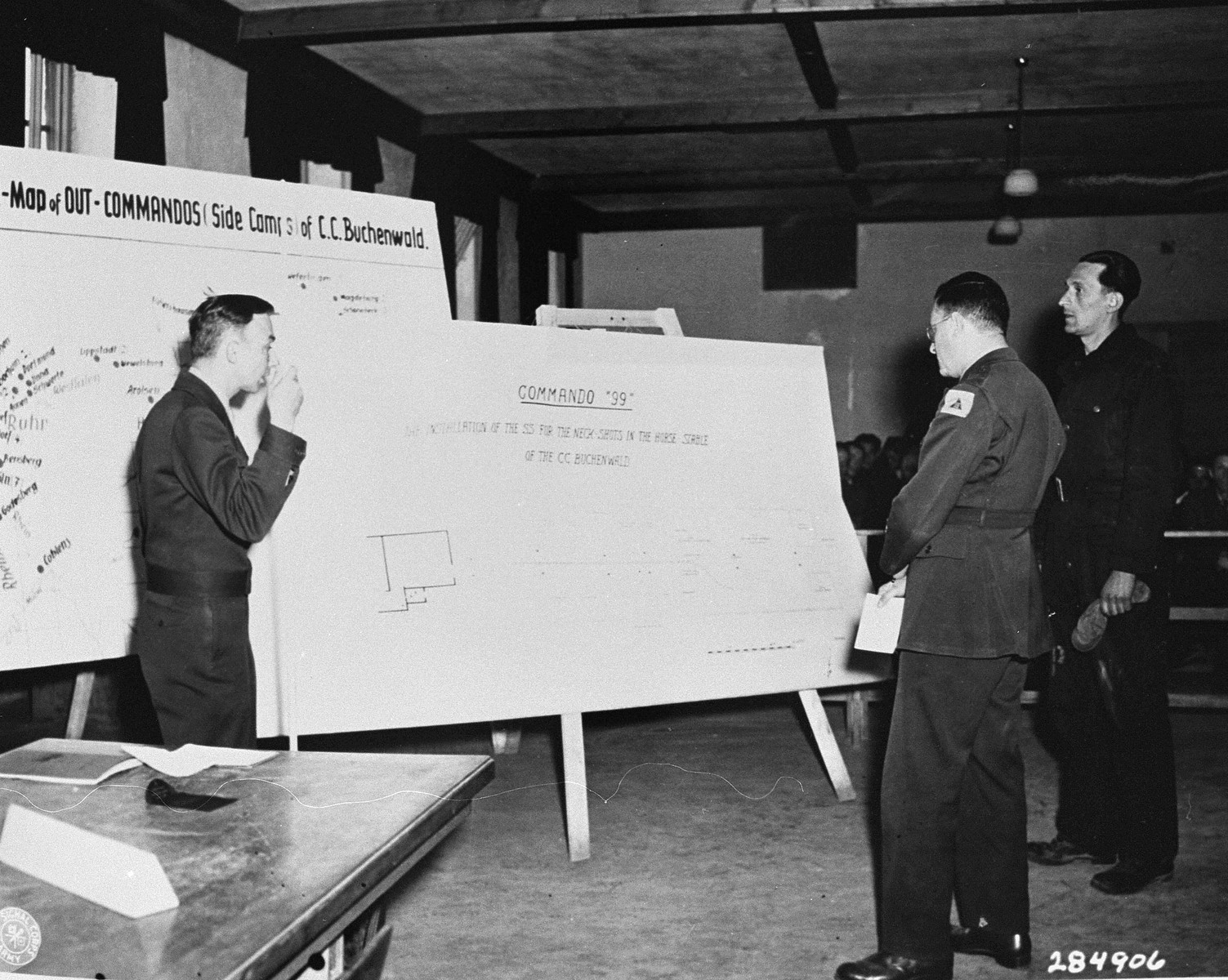 Horst Dittrich (right), a witness for the prosecution, identifies a diagram of a stable where prisoners were shot, at the trial of former camp personnel and prisoners from Buchenwald. 

Looking on are lead U.S. Prosecutor William Denson (left) and interpreter Rudloph Nathanson (center).