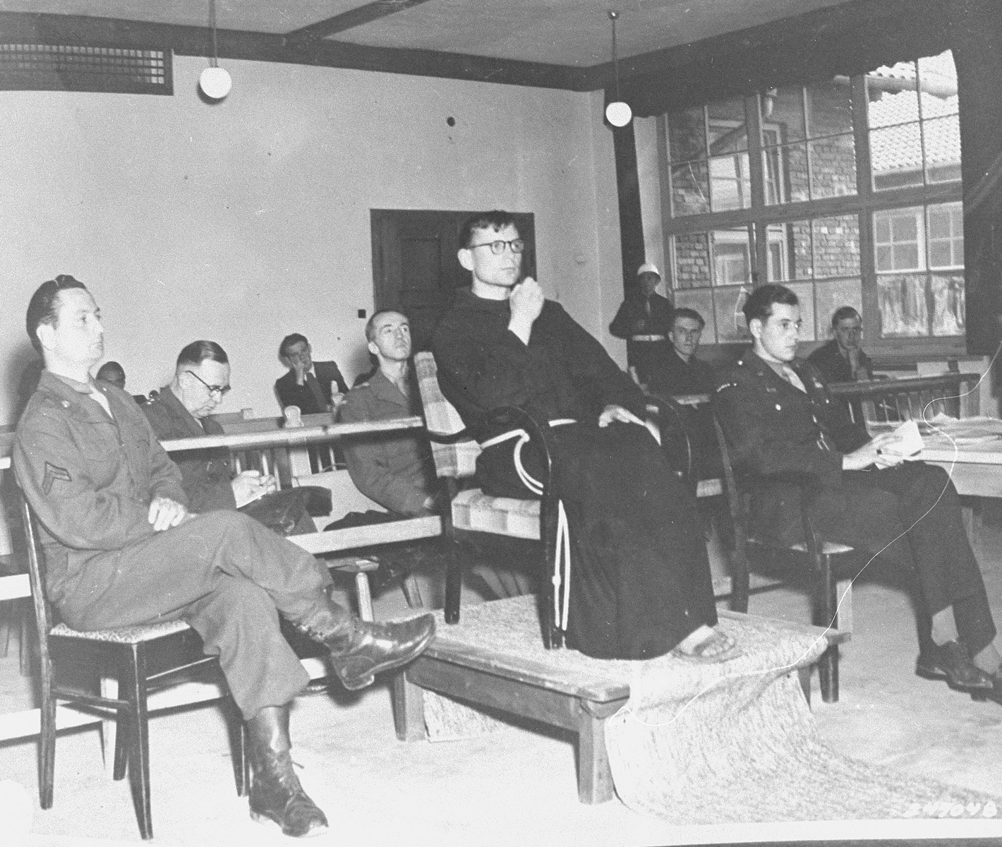 Father Louis Leclerc, a former prisoner, testifies at the trial of former camp personnel and prisoners from Flossenbuerg.  On the right is Fred Stecker, a court interpreter.