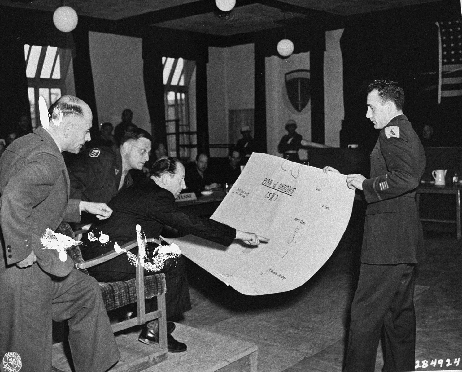 Dr. Viktor Abend, a Polish civilian witness for the prosecution at the trial of former camp personnel and prisoners from Buchenwald, points to a diagram of Ohrdruf, a sub-camp of Buchenwald.  

Court personnel pictured from left to right are Dr. Aheimer, a defense attorney; Rudolph Nathanson, an interpreter; Dr. Abend; and Sol Surowitz, an attorney for the prosecution.