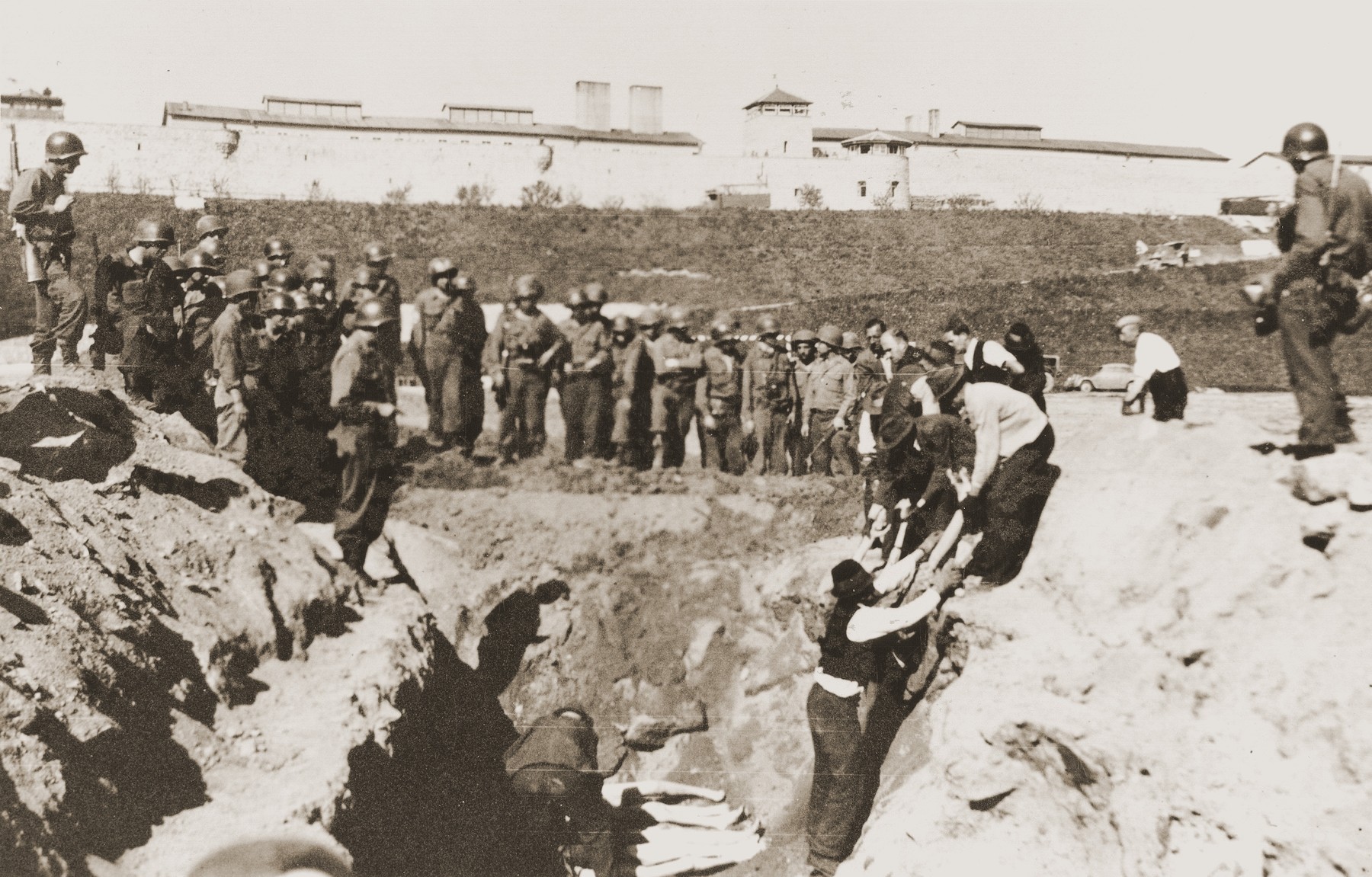 American soldiers watch as Austrian civilians lay the bodies of Mauthausen victims in a mass grave dug in the former SS soccer field.

Ray Buch stands at the right holding a camera.  Officers Chas Thurston of Pennsylvania and Harry Brown of Texas are among the American soldiers standing guard.