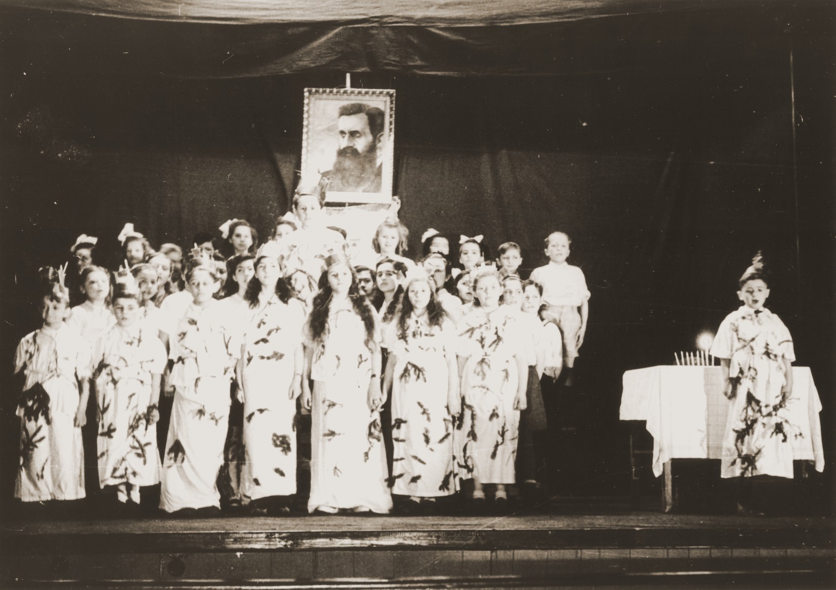 Children put on a Hannuka play in front of a portrait of Theodore Herzl in the Feldafing DP camp.