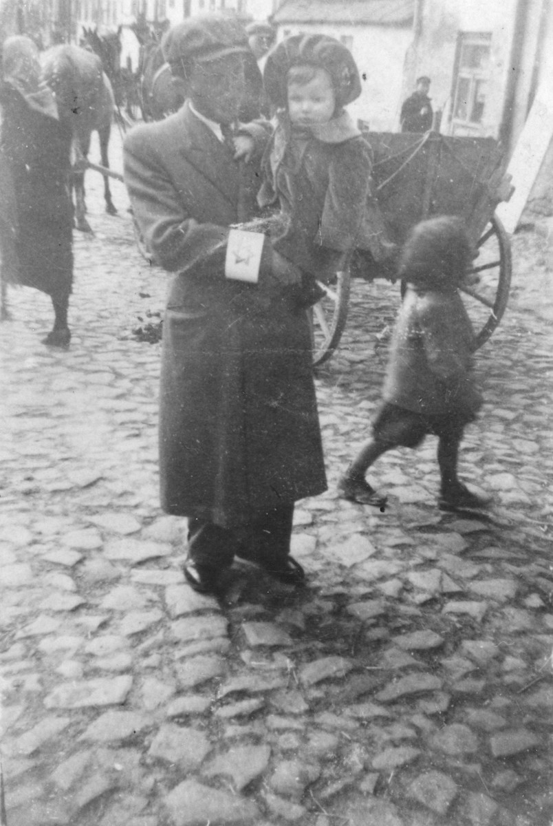 Majer Sztajman poses on a cobblestone street in the Opatow ghetto holding his baby daughter, Mania.