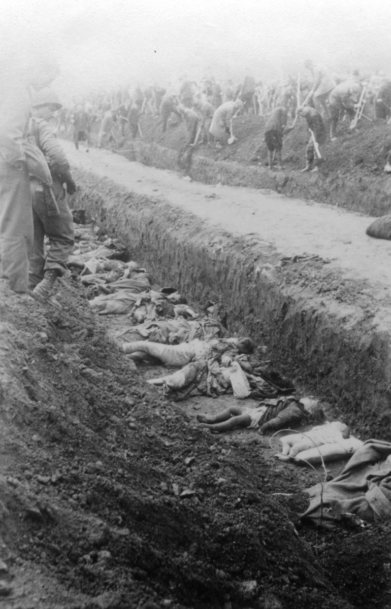 The bodies of prisoners killed in the Nordhausen concentration camp lie in an open mass grave.  

In the background, German civilians fill in another mass grave under the supervision of American troops.