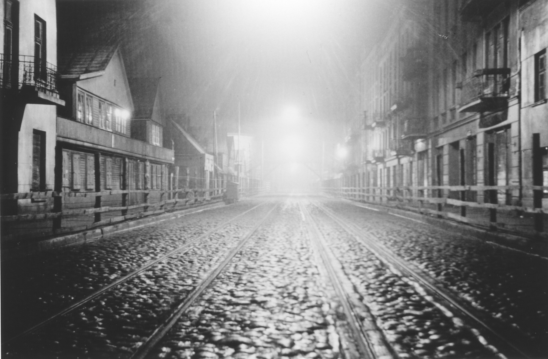 Night-time view of one of the thoroughfares that ran through the Lodz ghetto.

The photograph was probably taken by a member of Police Battalion 101.

The Lodz ghetto was divided into three sectors by two major throughfares which passed through, but did not belong to the Jewish district.  Wooden and barbed wire fences prevented access to these main streets by ghetto residents.  But Jews were allowed to traverse the streets by means of two wooden pedestrian bridges, accessed by steep staircases. 

One image from a photograph album belonging to a member of Police Battalion 101.