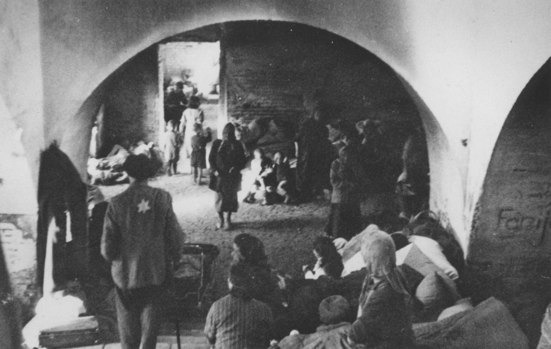 Jews wearing Stars of David sit beneath arched ceilings in a multi-room cellar in an unidentified ghetto. 

One image from a photograph album belonging to a member of Police Battalion 101.