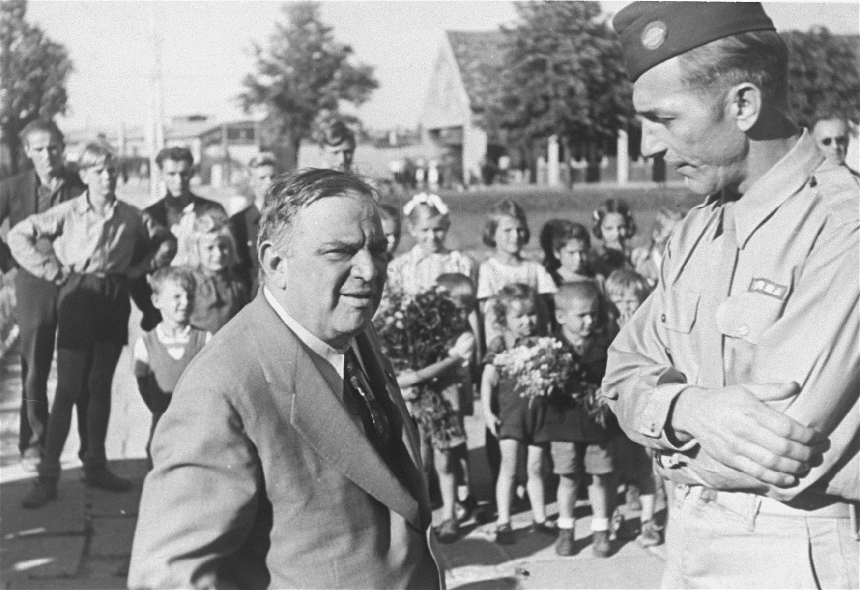 UNRRA Director General Fiorello LaGuardia converses with an unidentified official during a visit to the Neu Freimann displaced persons camp.

In the background a group of children stand in formation.