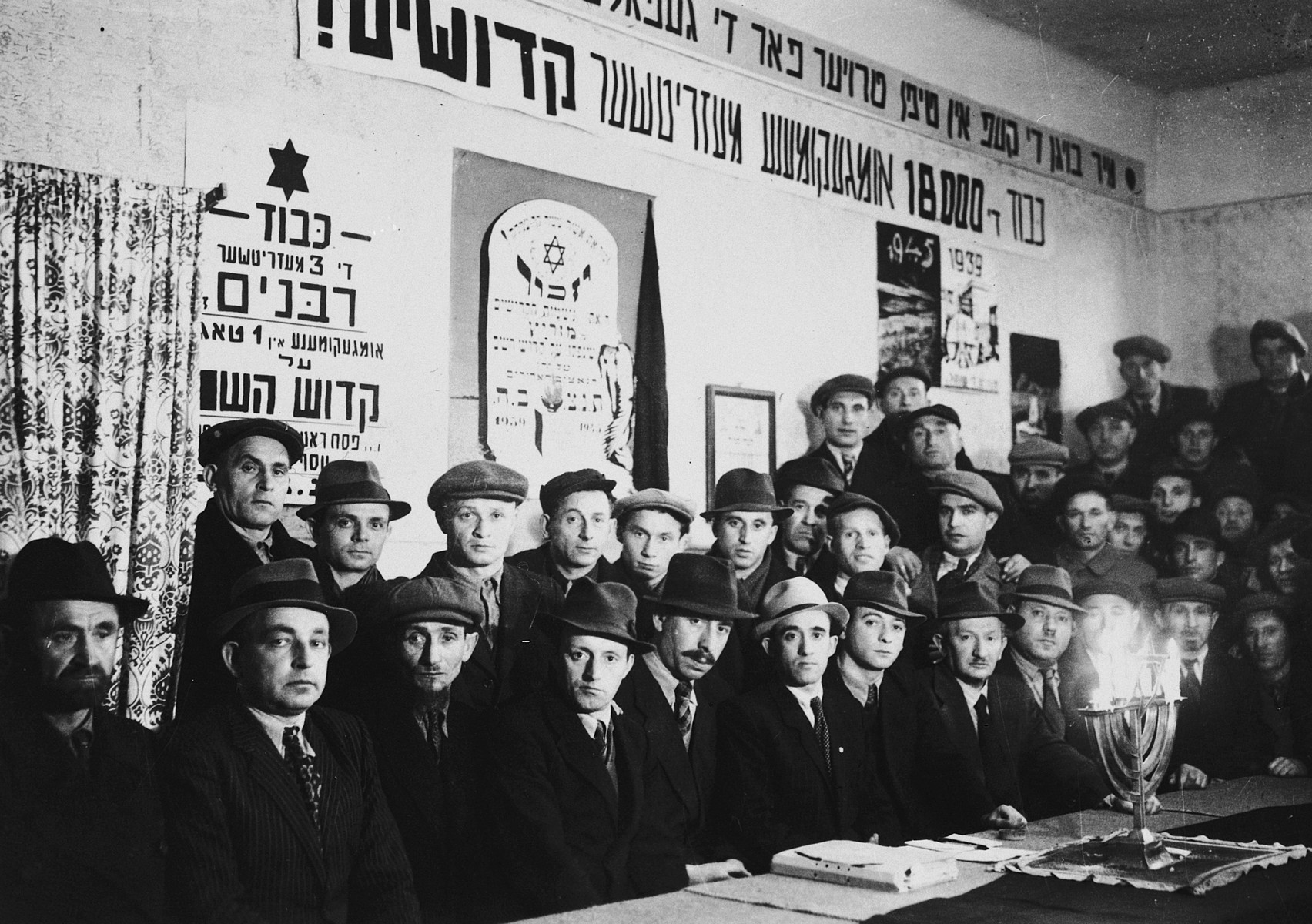 Jewish DPs gather for a service to commemorate the Holocaust victims from Miedzyrzec Podlaski underneath banners memorializing the victims.

Among those pictured is Cantor Pinchos Rabinowitz who officiated at the service.