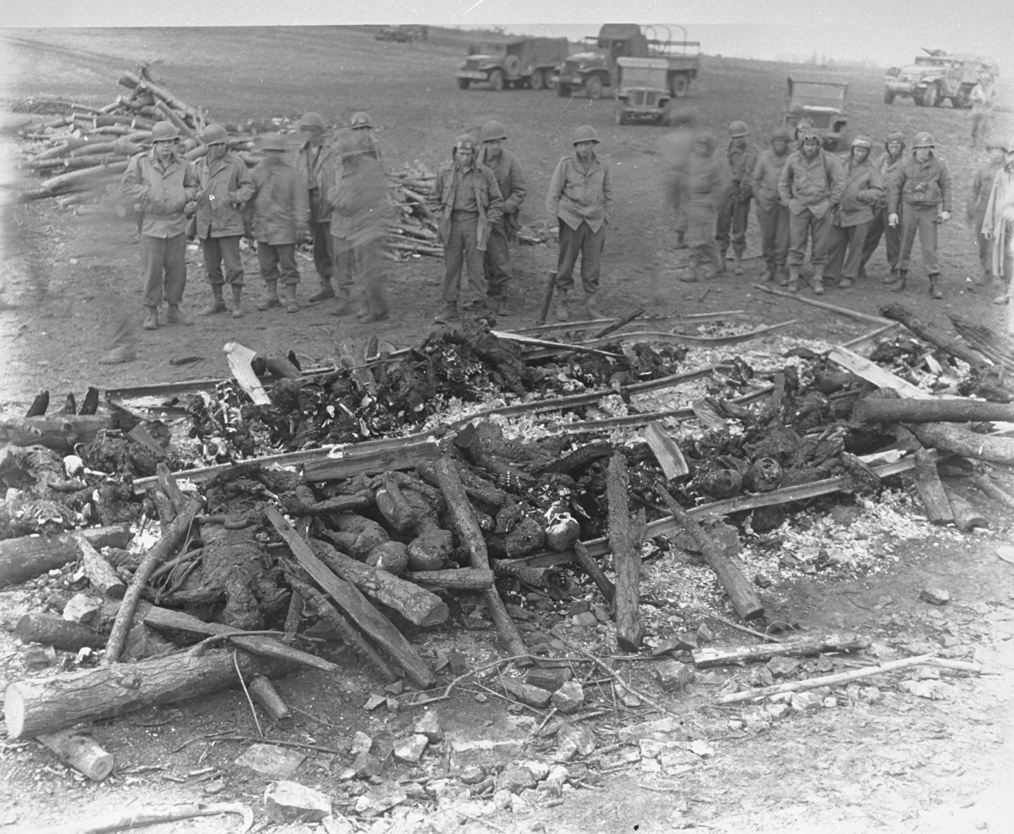 While on an inspection tour of the newly liberated Ohrdruf concentration camp, American soldiers view the charred remains of prisoners that were burned upon a section of railroad track during the evacuation of the camp.

The original caption reads "The charred remains of burned prisoners are shown shortly after capture of the area by Third U.S. Army troops.  The Nazis exhumed and burned 1,606 murdered victims in six days in an attempt to destroy the evidence on orders from higher headquarters."

From left those pictured are Nylan Ellsworth, George Stantis (second from left, tentative identification), Jack Caminer (fifth from left with goggles), a German-Jewish immigrant, who served in military intelligence.  The man standing alone in the middle, eighth from the left, has been identifed as Staff Sergeant  Maynard B. Cohen or Americo Venuto or Richard Wolff.  Captain Ralph Kopansky is pictured on the far right, with a camera around his neck.
