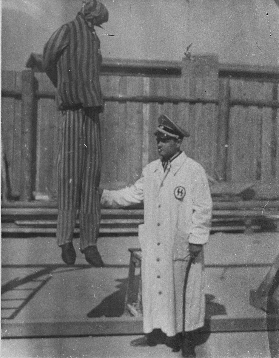 A man posing as a member of the SS stands next to the simulation of an execution by hanging.
