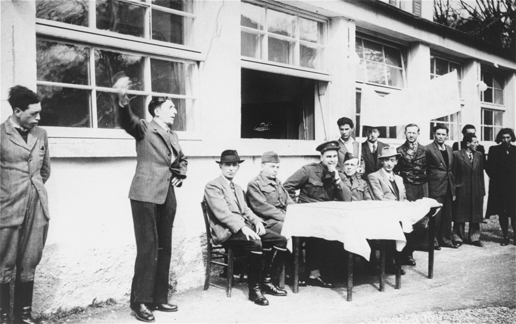 Jewish DPs in the Mittenwald displaced persons camp conduct a meeting at which they protest British immigration policy to Palestine while they commemorate the death march from Dachau to Tyrol.

Among the participants is Mr. Spier, an UNRRA representative.