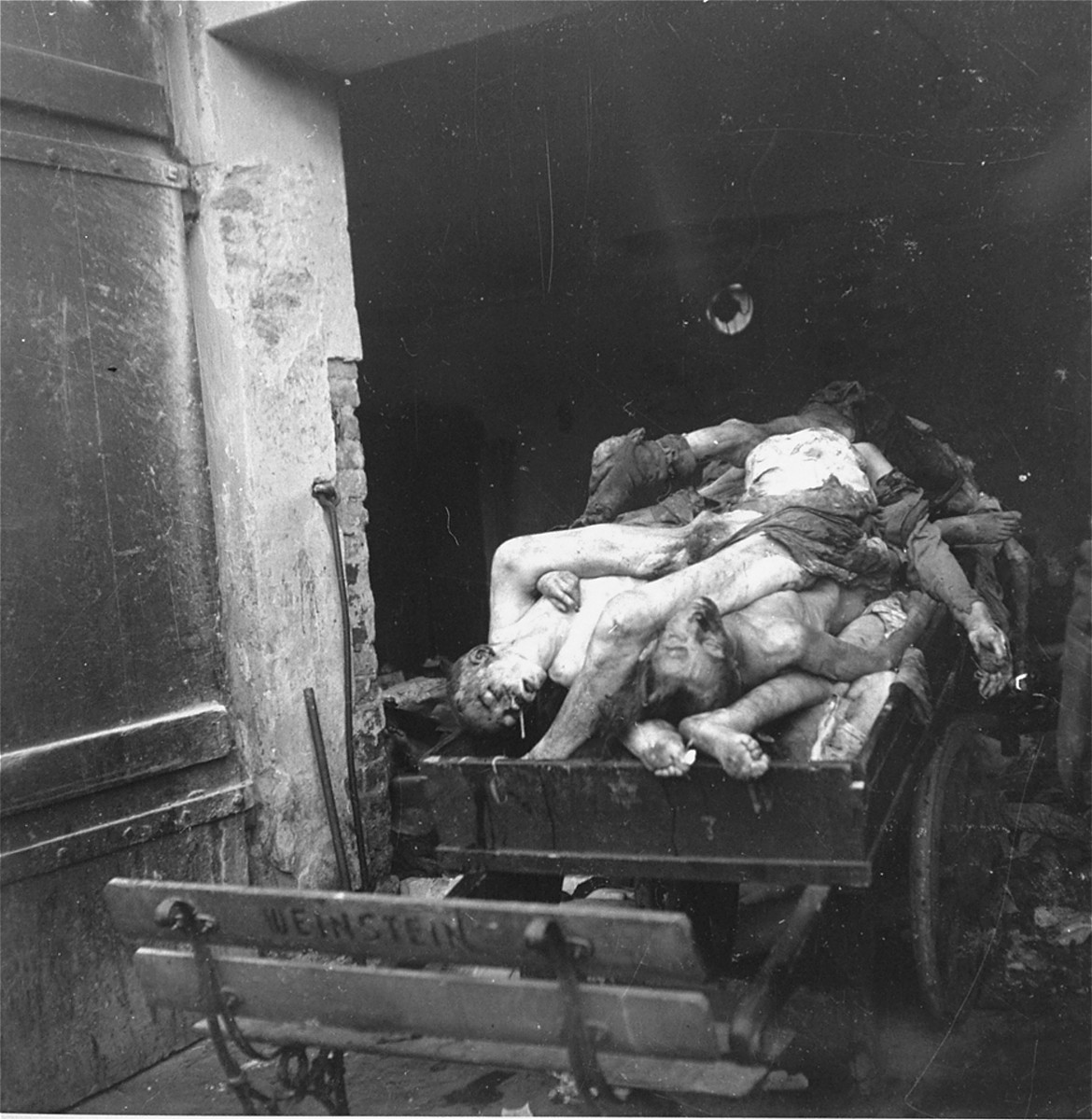 A corpse-laden wagon stands just inside the morgue of the Jewish cemetery on Okopowa Street in the Warsaw ghetto.  

Joest's caption reads: "One of the corpse-bearers opened the door of the shed so I could take photos.  It was an unsettling picture."