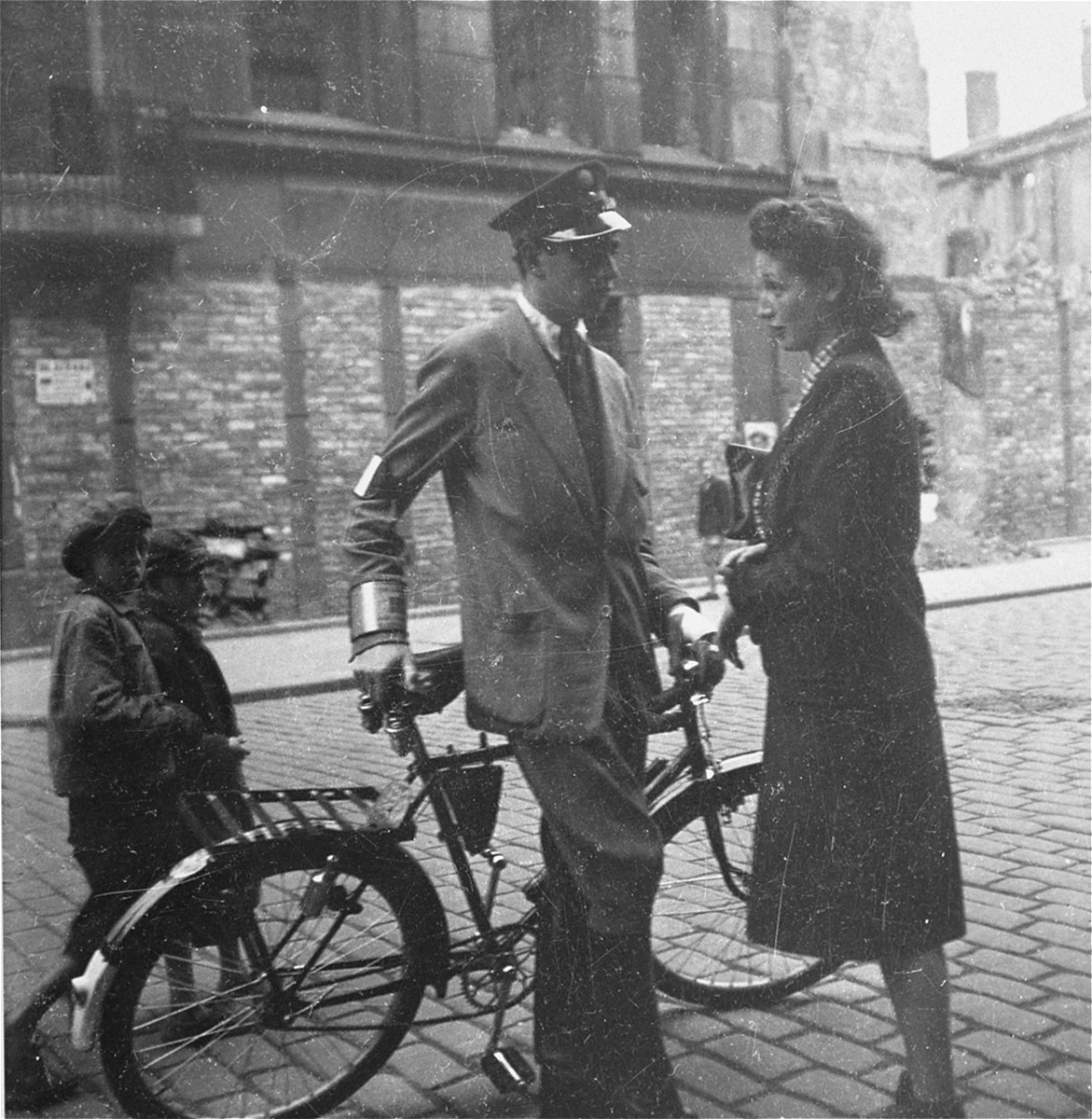 A Jewish policeman speaks with a woman on the street in the Warsaw ghetto.  

Joest's captions reads: "It looked like a flirtation, this brief encounter between a young woman and the handsome policeman, but the begging children in the background provided a contrast."