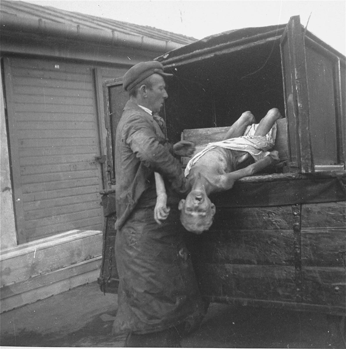 A workman pulls a corpse from a funeral wagon for burial in the Jewish cemetery on Okopowa Street.  

Joest's caption reads: "I thought at first that this dead person was a small child, but the body had gray hair."