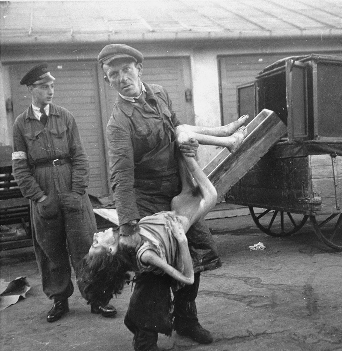 An undertaker in the Warsaw ghetto's Jewish cemetery on Okopowa Street lifts the body of a woman for Heinrich Joest to show him how little it weighs.  

Joest's caption reads: "The dead were not heavy, as one corpse-bearer showed me - although I had not asked him to - in front of the buildings of the Jewish cemetery."