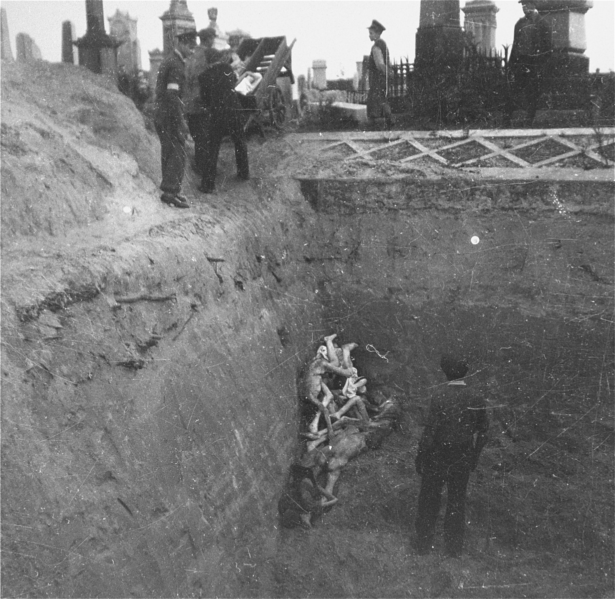 Undertakers from the funeral home of M.B. Pinkiert unload bodies from a cart into a mass grave in the Warsaw ghetto cemetery.  

Joest's caption reads: "Like household trash thrown into a ditch, these corpses of people alive only a short time before, were here dumped into the grave before my eyes."