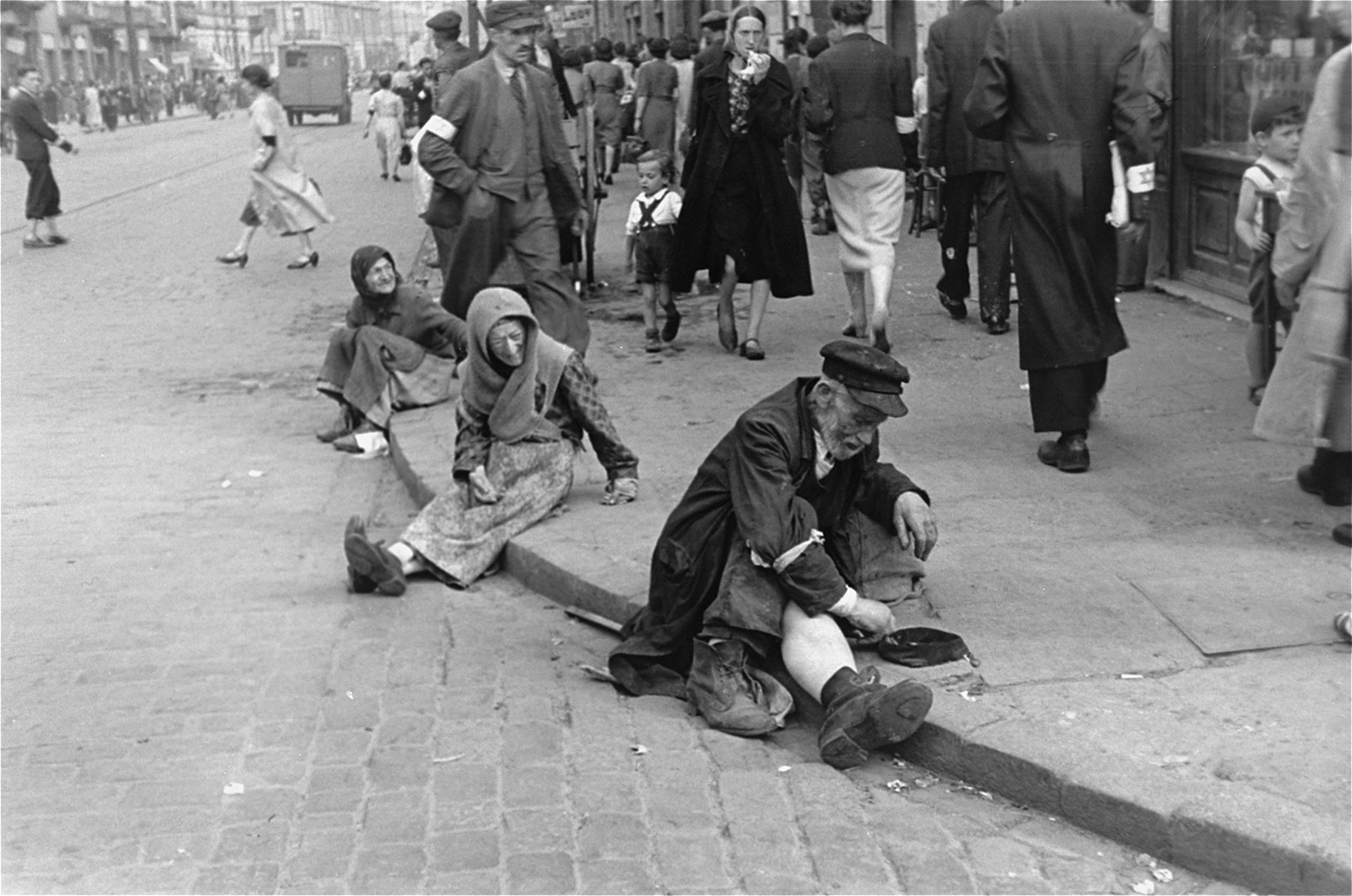 Destitute Jews sit on a street corner in the Warsaw ghetto begging for assistance.