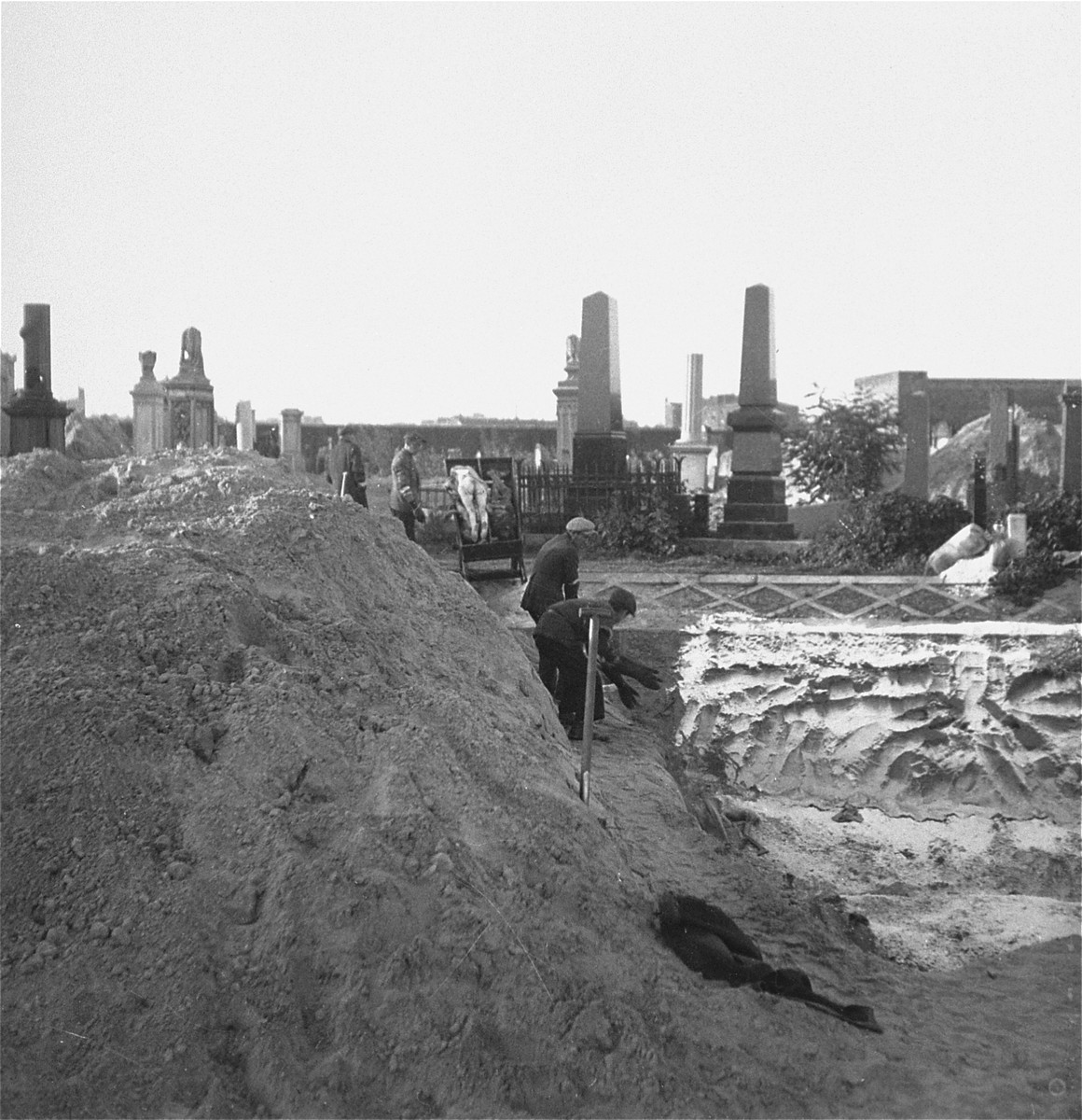 Gravediggers unload bodies from a cart into a mass grave in the Warsaw ghetto cemetery.  

Joest's caption reads: "The corpse-carriers took the naked bodies from the cart and threw them into the grave.  For this work they wore rubber-gloves, which I first thought were made out of wood."