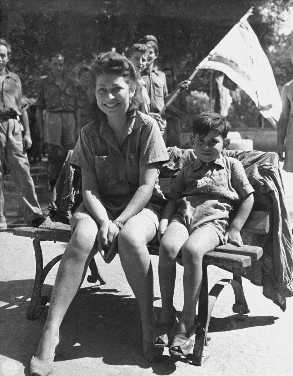 Stella Aojne, a former nurse with the Yugoslav Partisan Army, and her son, Ivol, await transportation to the port of Naples, where they will board a ship to Palestine. 

Stella's husband was killed while fighting with the Partisans.