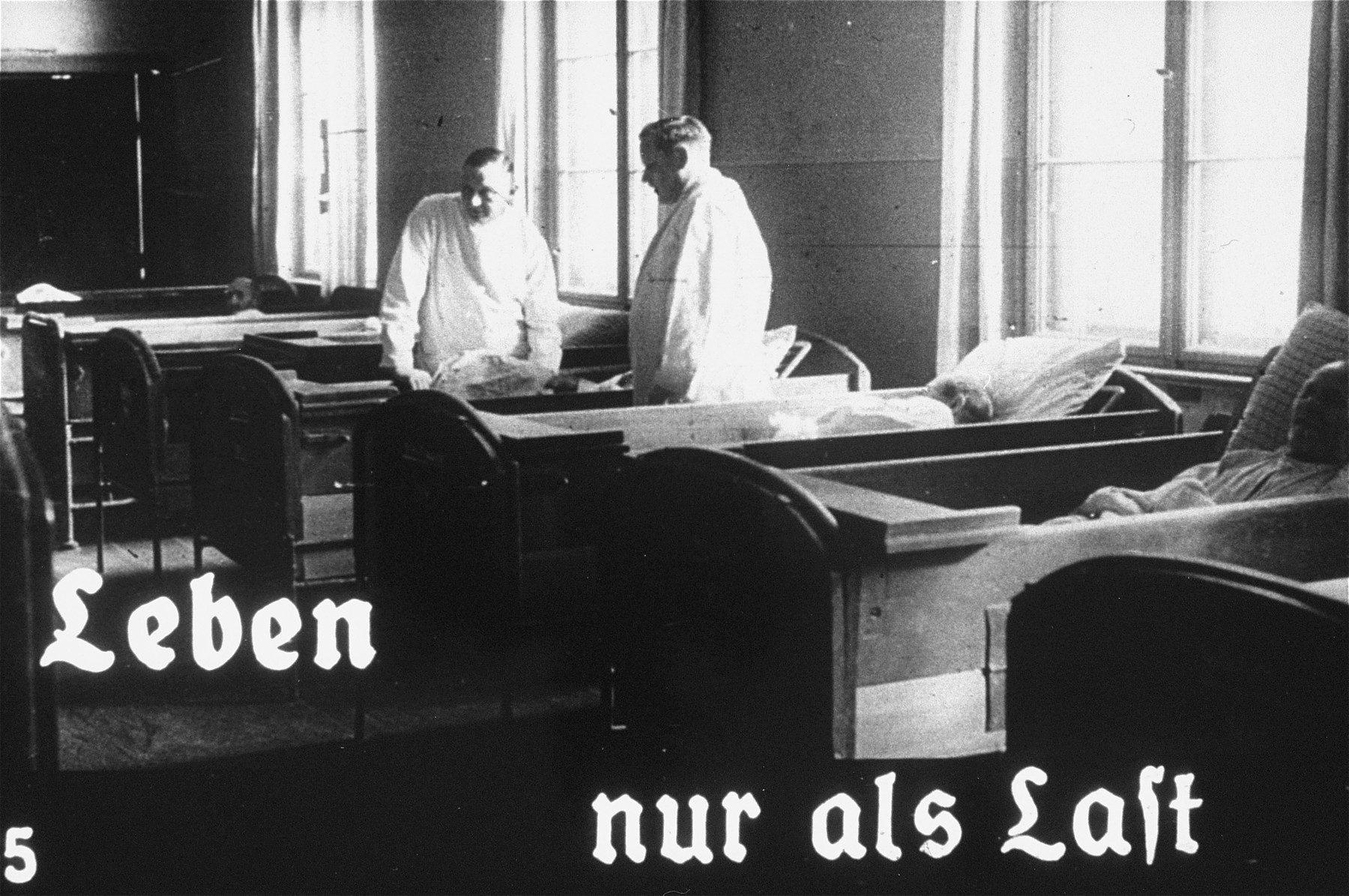 Propaganda slide featuring two doctors working at an unidentified asylum for the mentally ill.  The caption reads, "Life only as a burden."