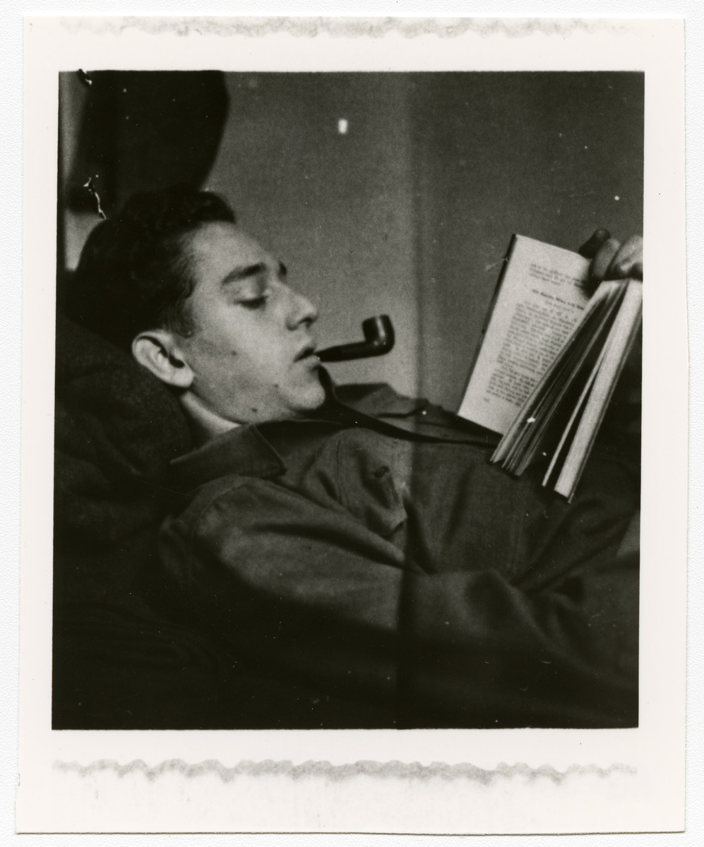 American GI Lee Merel relaxes by reading and smoking a pipe.