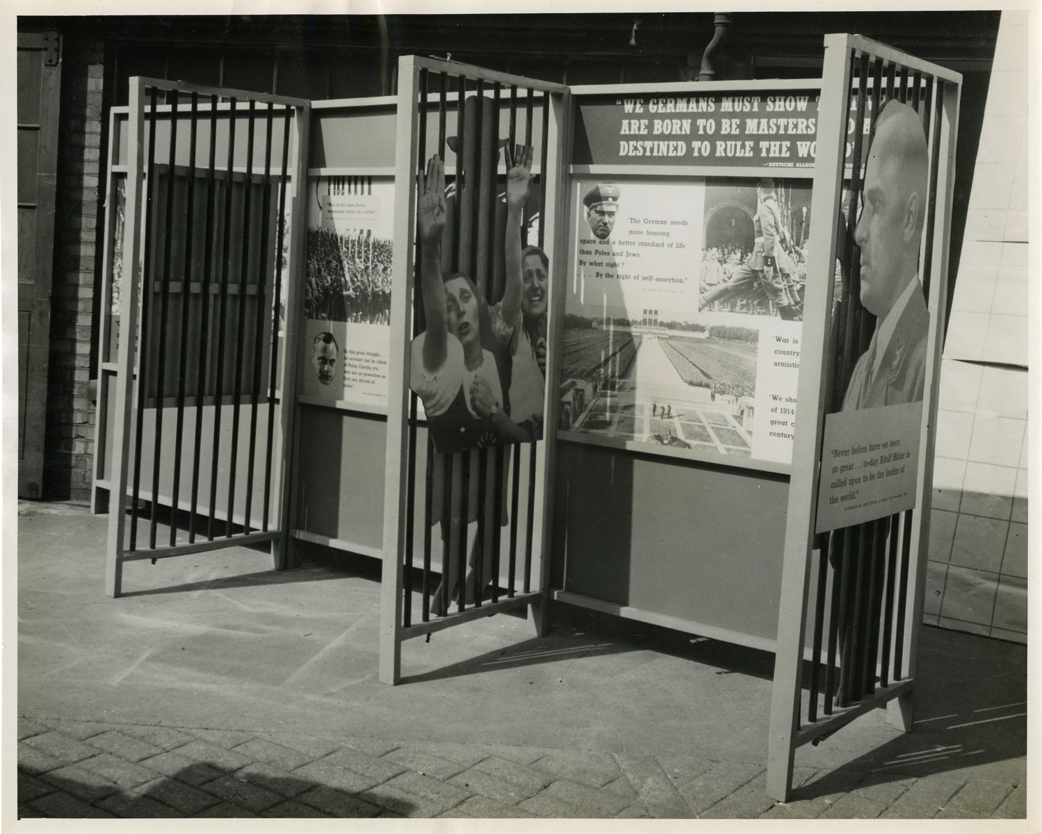 Panel from a 1944 exhibition in London, England, entitled "Germany- the Evidence." 

Quote from the panel reads "We Germans must show that we are born to be masters [and are] destined to rule the world." 

The back of the photo reads "British Official Photograph; Distrbuted by the Ministry of Information. D. ; The Evil We Fight.; Ministry of Information Exhibition priduced by Display & Exhibitions Division for show all over Great Britain.; Display panel"