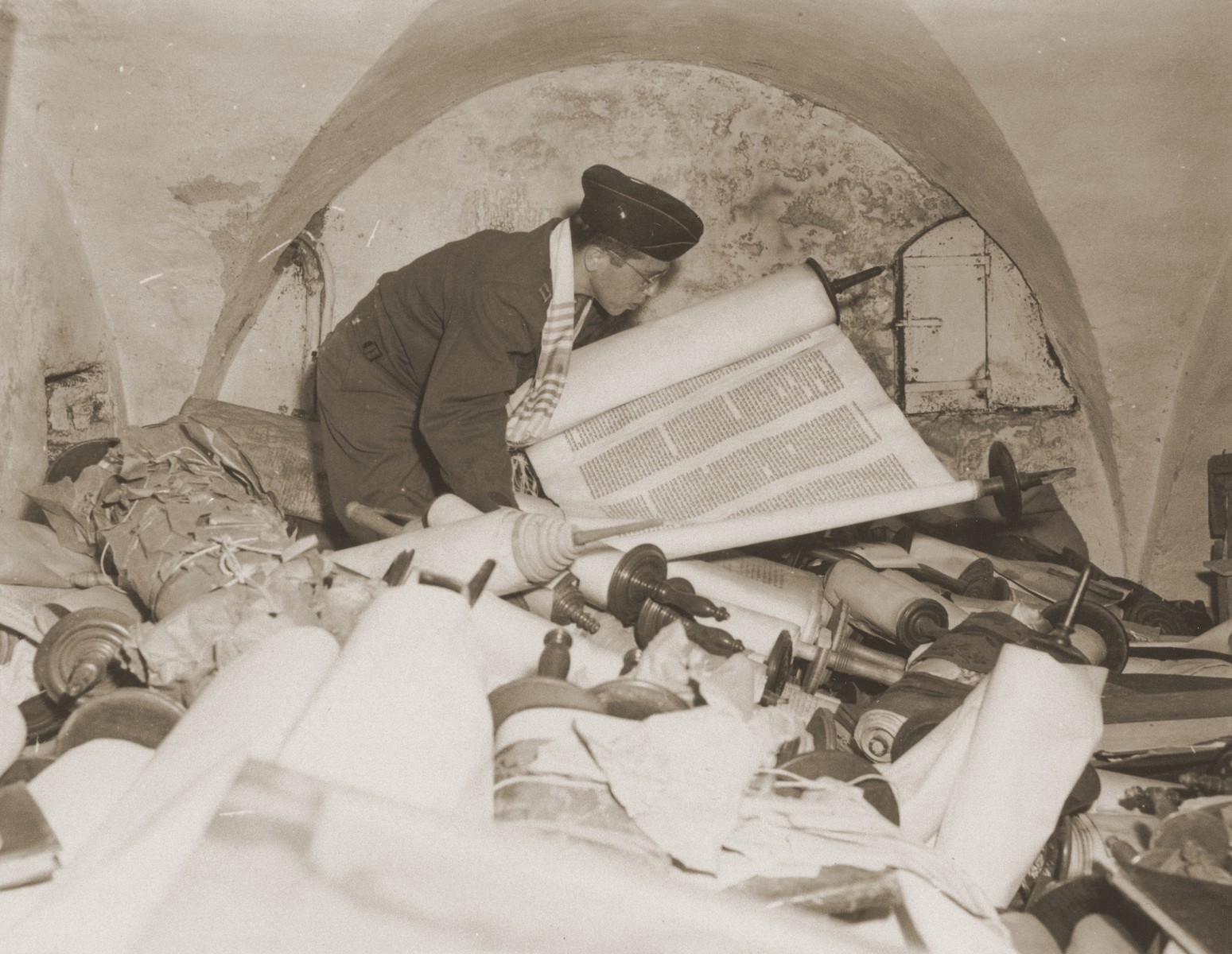 Chaplain Samuel Blinder examines one of the Torah scrolls stolen by the Einsatzstab Rosenberg and stored in the basement of the Institut fuer Juedische Erforschung [Institute for Research into the Jewish Question] in Frankfurt am Main.

The Einsatzstab Rosenberg, established by Reichsleiter Alfred Rosenberg in 1941, travelled to newly occupied countries and confiscated materials from libraries, archives, and private homes.  In this manner, the Institut fuer Juedische Erforschung quickly amassed a library of over 40,000 books.