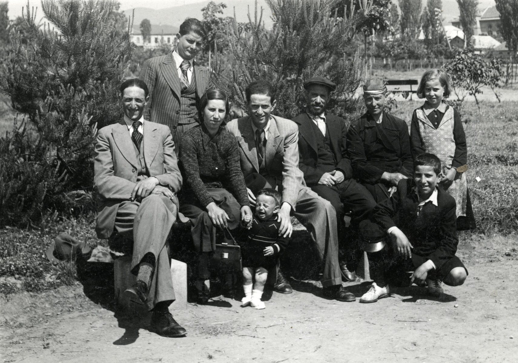 A group of eight people and a baby pose on and around a park bench in Bitola. 

The couple sitting on the right of the bench are the parents of Rabbi Moise Cassorla.