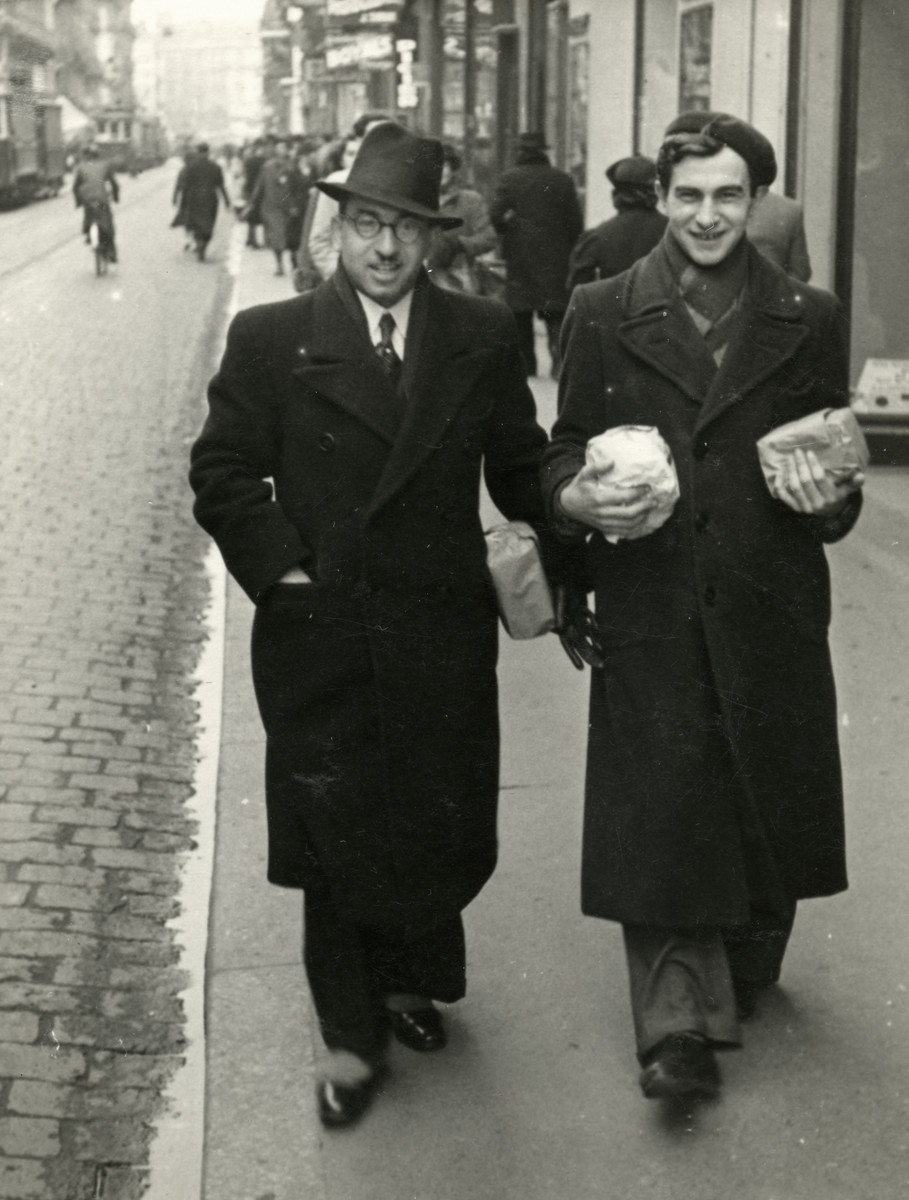 Rabbi Moise Cassorla and Chief Rabbi Paul Roitman walk down a street of Toulouse carrying paper-wrapped packages. 

The inscription on the back of the photograph reads, "Toulouse Pourim 1941".