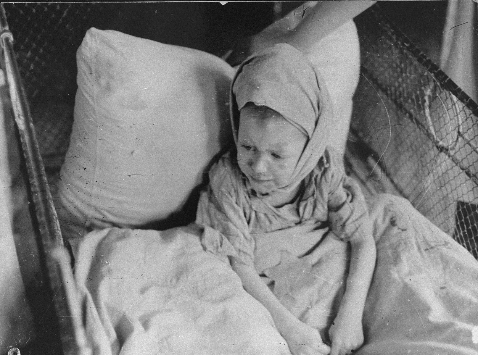A sick child sits in a crib in the Kovno ghetto hospital, covered by a blanket with a Star of David.