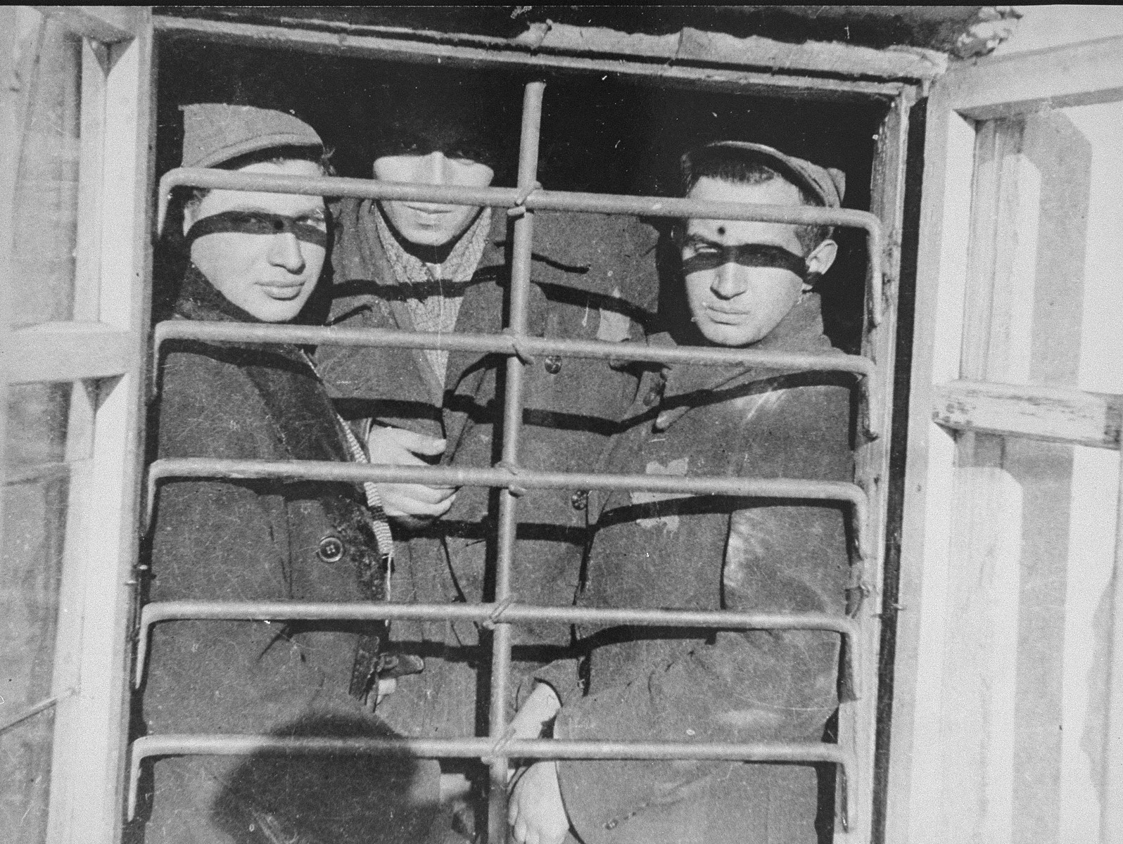 Three men behind a barred window in the ghetto jail.