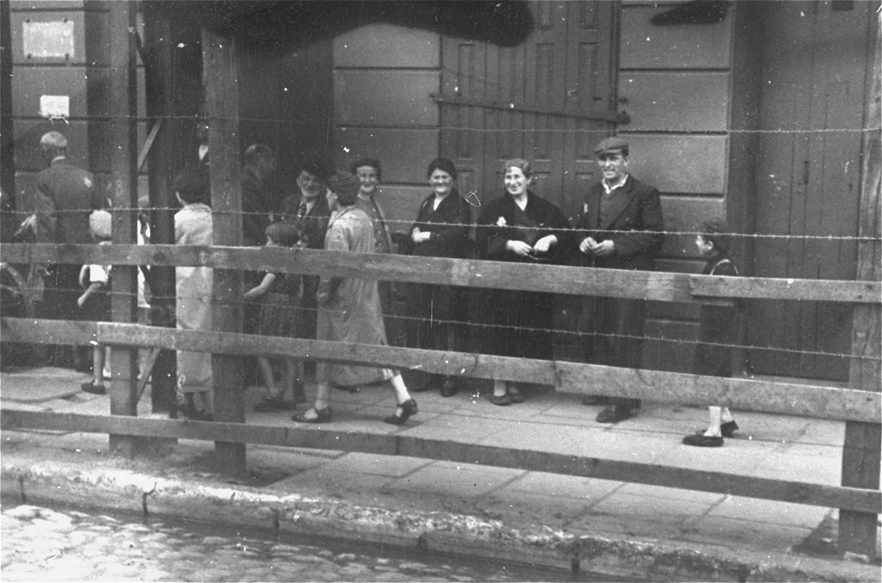 Lodz ghetto Jews behind the wooden and barbed wire fence that separated the Lodz ghetto from the rest of the city (probably taken from Zgierska Street).