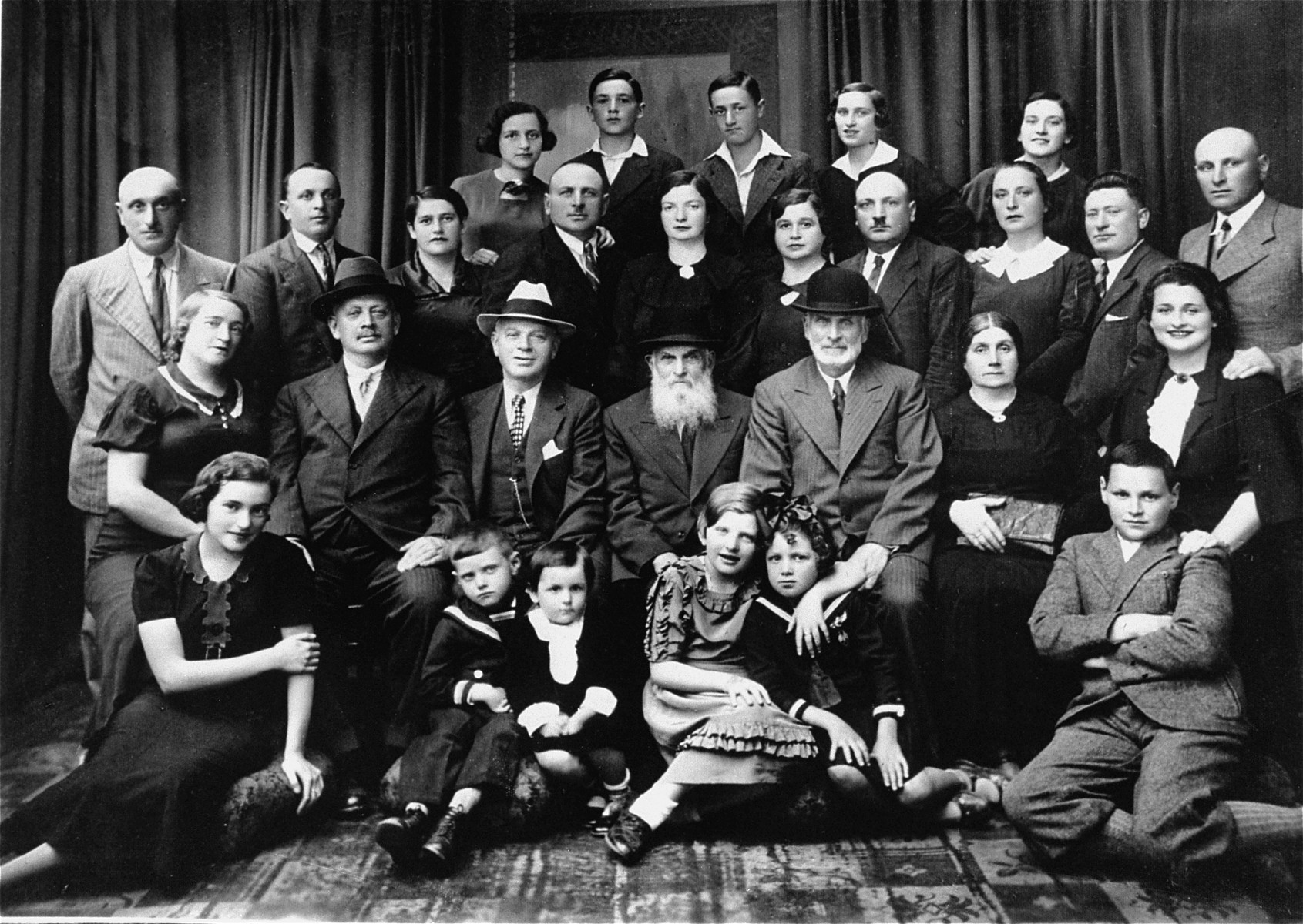 Group portrait of members of the Solski family taken during a family gathering in honor of two visiting great uncles, one from South Africa and one from America.

Rella Solski is the child pictured in the front row in the sailor suit.  Rella Solski (donor) and her cousin, Mina Braudh were the only survivors. 

Bottom row, left to right
Moshe Solski
Label Solski
Rella Solski, daughter of Chatzkel
Eta Rella, cousin of donor
Rella, donor
Kera Solski, cousin of donor

Second row from bottom, left to right
Dina Solski, aunt of donor, Peretz's wife
Wolf Solski, uncle from South Africa
Joe Saul, uncle from United States
Zusal Solski
Abe-y Solski, donor's grandfather
Donor's step-grandmother
Mania Solski, wife of Solomon

Third row from bottom, left to right
Peretz Solski, donor's uncle on father's side, husband of Dina
Chatzkel Solski, donor's uncle on father's side
Chaja Solski, donor's aunt, pregnant in picture
Joe Solski, husband of Gita, father of Label and Eta Rella
Gita Solski, wife of Joe Solski, mother of Label and Eta Rella
Dina Solski, donor's mother
Zusel Solski, donor's father
Rivka Braudh, donor's aunt on father's side
Alter Braudh, Rivka's husband
Solomon Solski, Mania's husband

Fourth row from bottom, left to right
Mina, daughter of Dina and Peretz
Charles, brother of donor
Label, son of Dina and Peretz
Brira Braudh, son of Rivka and Alter
Mina Braudh, daughter of Rivka and Alter