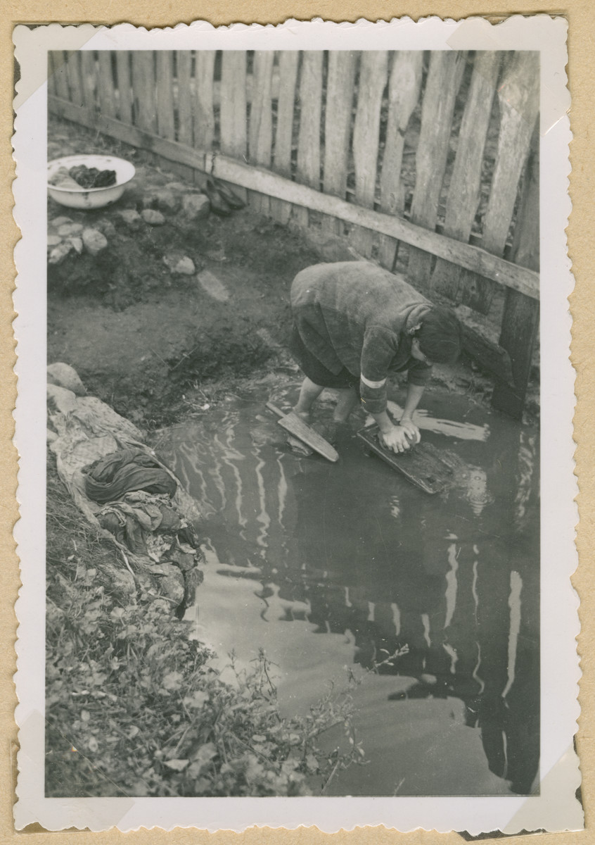 A Jewish woman wearing an armband washes clothes outside in an unidentified ghetto in Poland.