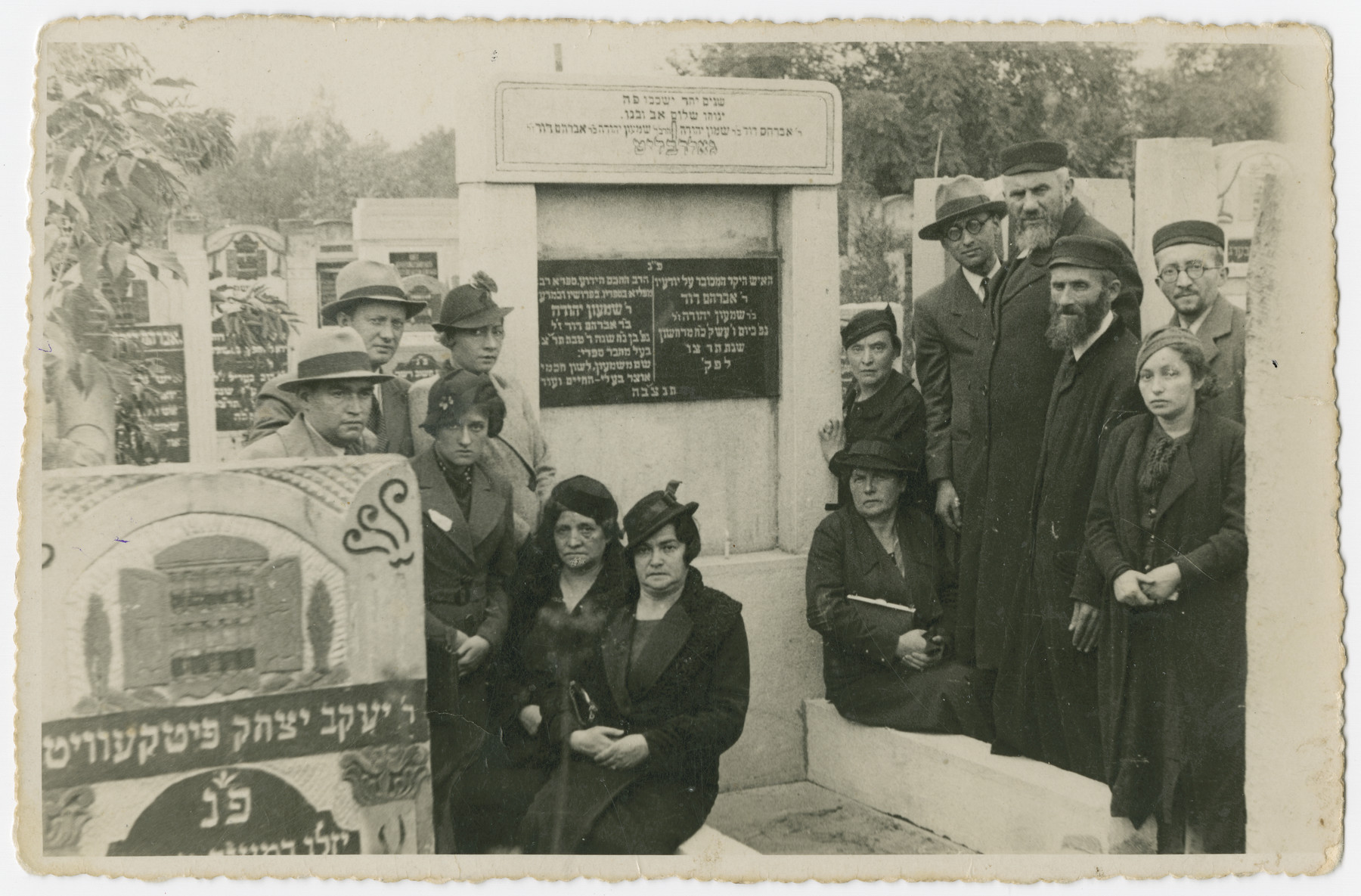 An extended Polish Jewish family gathers by a tombstone in the Jewish cemetery in Lodz.

Herschel Hudes (father of Lola Hudes Bielski), standing fourth from right and Necha Hudes (mother of Lola Hudes Bielski), seated first from left are pictured at the Lodz Cemetery shortly before the Holocaust.  All the people in the photo perished in the Holocaust.