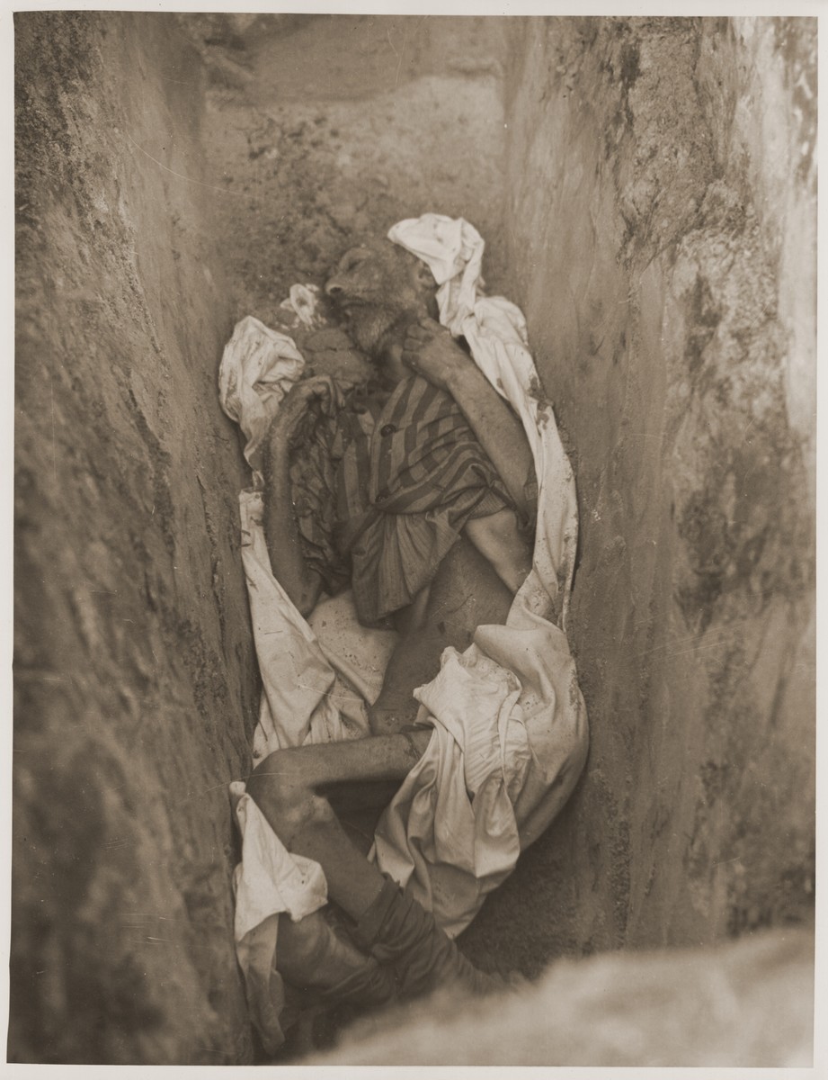 The emaciated corpse of a prisoner that is partially wrapped in a sheet, lies at the bottom of a grave in the newly liberated Woebbelin concentration camp.