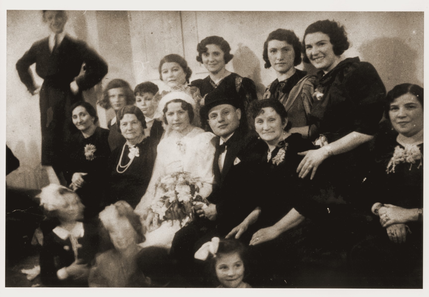 Group portrait of family and friends at the wedding of Bracha Broncia Rotsztajn and Mr. Kratka.  

Standing on the far left is Aaron Rotsztajn (the donor's paternal uncle, who escaped Poland to Palestine in 1941).  In the second row, second from the left, is Roma Rotsztajn (the donor), her brother, Dawid; an aunt; Bracha Rotsztajn; Rozia Rotsztajn and Ela Rotsztajn.  In the front row, second from the left is Malka Rotsztajn (the donor's great grandmother); Bracha and her husband and Dwora (Rozmaryn) Rotsztajn (the donor's grandmother).  Aaron and Roma were the only survivors of this group.