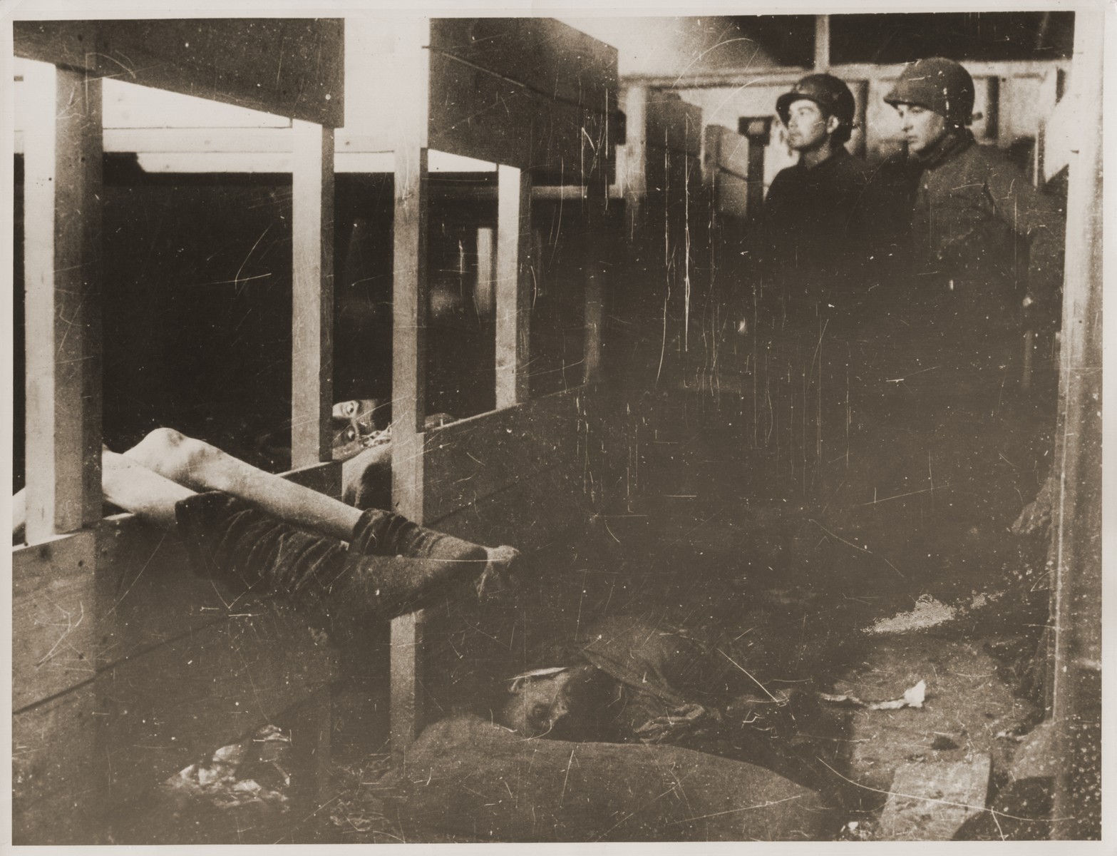 American troops inspect a barracks in Dora-Mittelbau soon after the liberation.  Two survivors lie in bunks, while corpses lie on the floor.