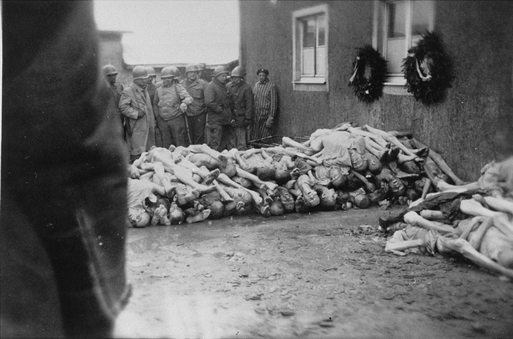 Survivors and American soldiers look at a pile of corpses behind the crematorium in Buchenwald.