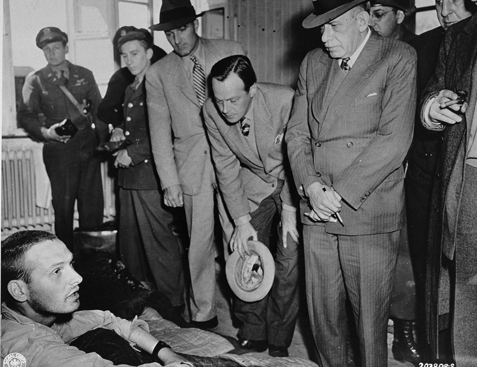 American newspaper editors visit a hospital in the newly liberated Buchenwald concentration camp to speak with survivors about the crimes they witnessed.  

Pictured from left to right are: Norman Chandler of the L. A. Times, William I. Nichols of This Week Magazine, and Julius Ochs Adler of the New York Times.