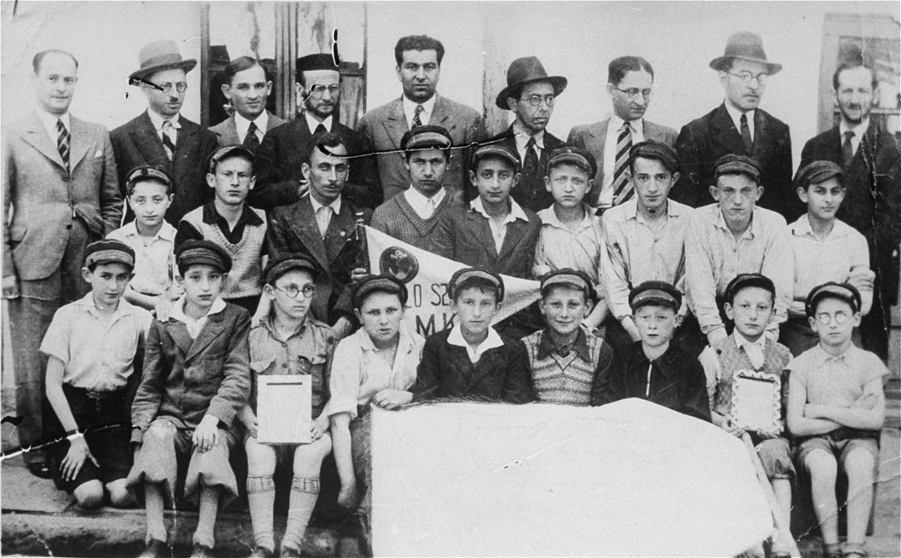 Group portrait of students and teachers of the Yavne Jewish religious elementary school for boys in Bedzin. 

Among those pictured are: Motek Rechnic (second row from the front, third from the right) and Hesiek Zvi Rechnic (second row from the front, fifth from the right). Both of these children were from Dabrowa Gornicza.