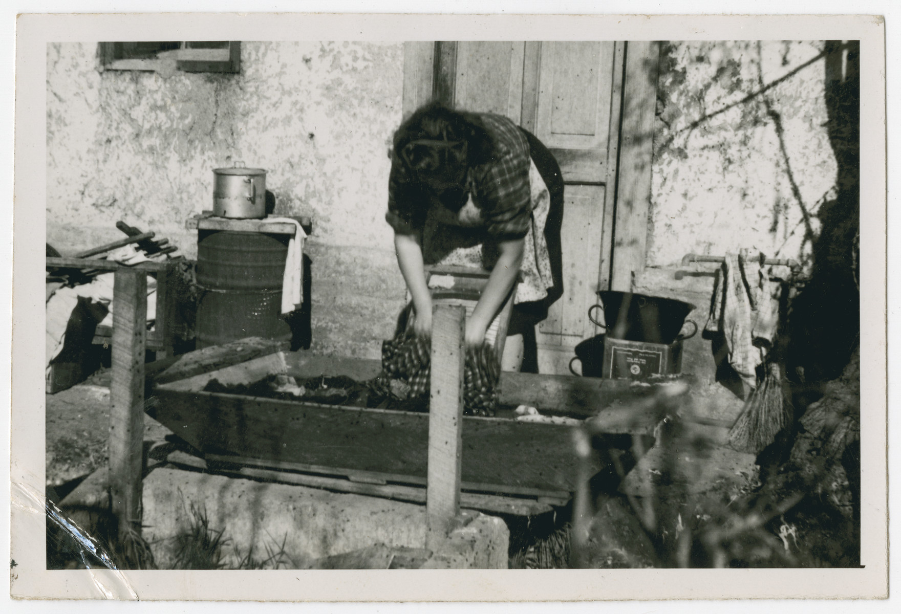 Photograph from an album entitled, "Hacshara Kidma Chile,"  documenting life on a postwar Shomer Hatzair Zionist agricultural collective in Chile.

A young woman washes clothing on a washboard. The inscription on the album page reads, "La Monja."