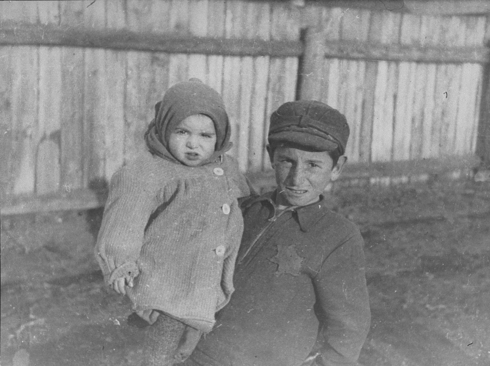 A young boy holding his younger brother in the Kovno ghetto.  

Older children frequently cared for younger siblings in the ghetto. 

The caption written on the back of the photograph by George Kadish (translated from Yiddish) reads, "Two orphan brothers in the Kovno ghetto."